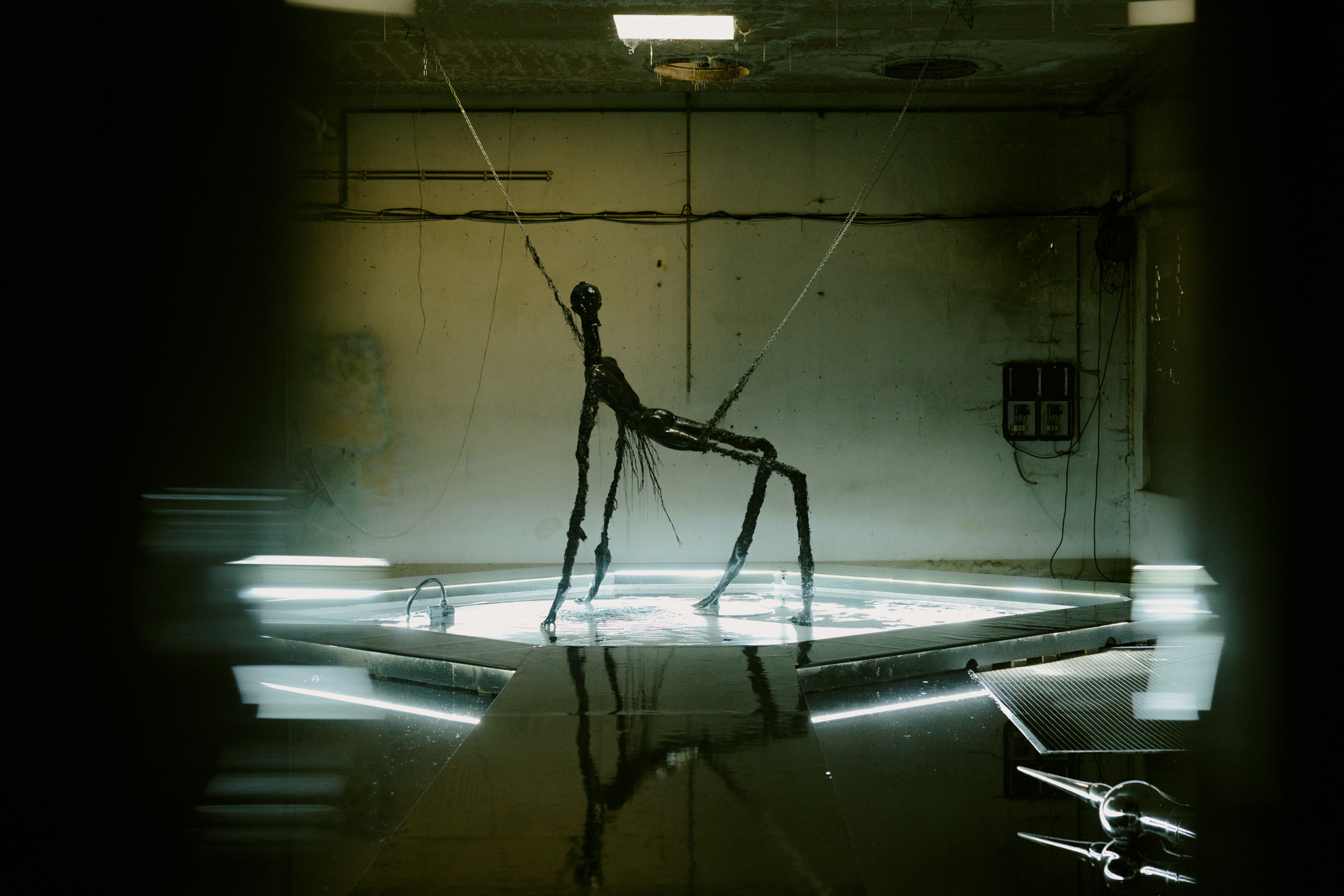 A tall, elongated figure cast in shadow stands on a reflective surface, creating an eerie, surreal image.