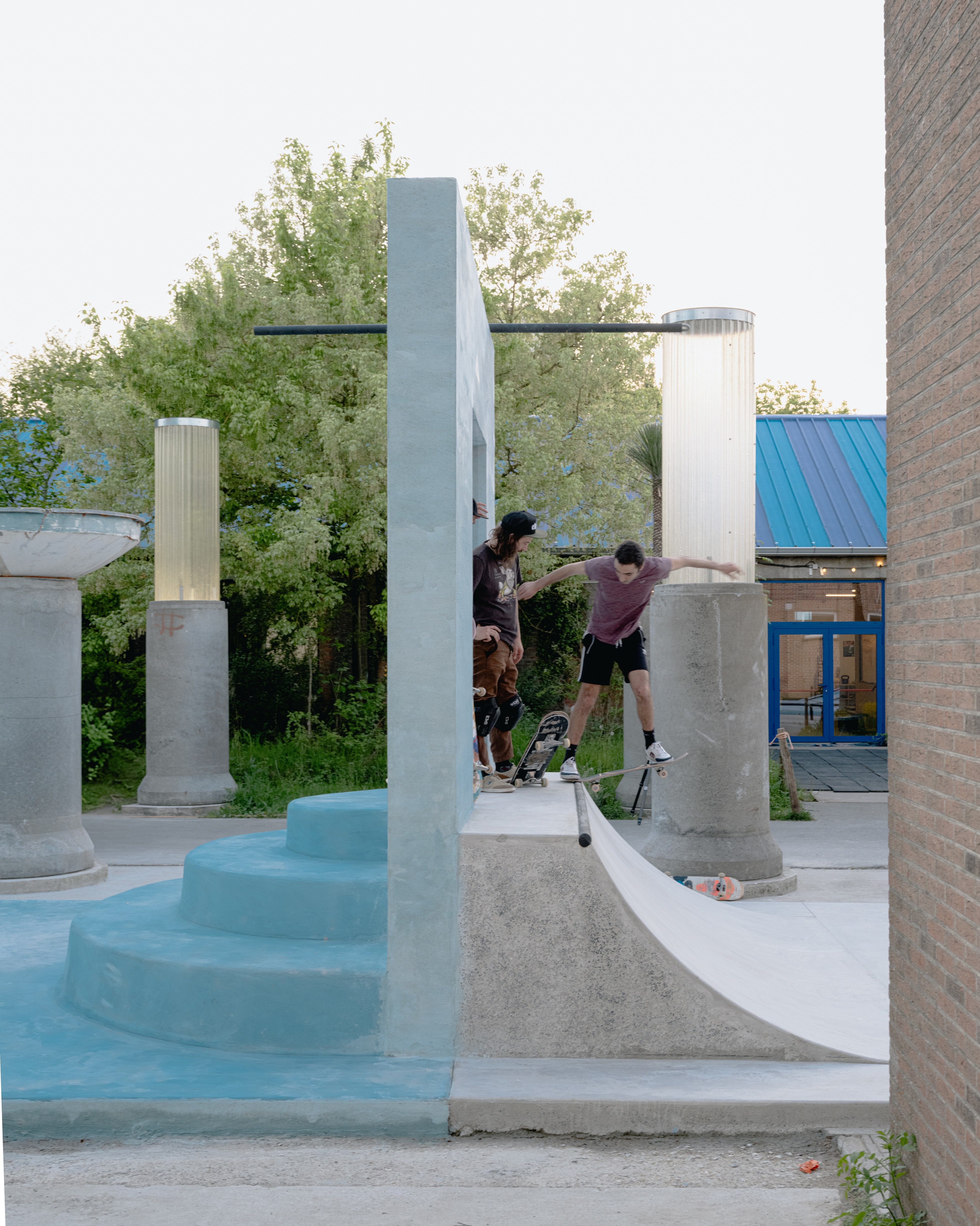 Concrete skate park with ramps and graffiti-covered walls, surrounded by greenery and trees.