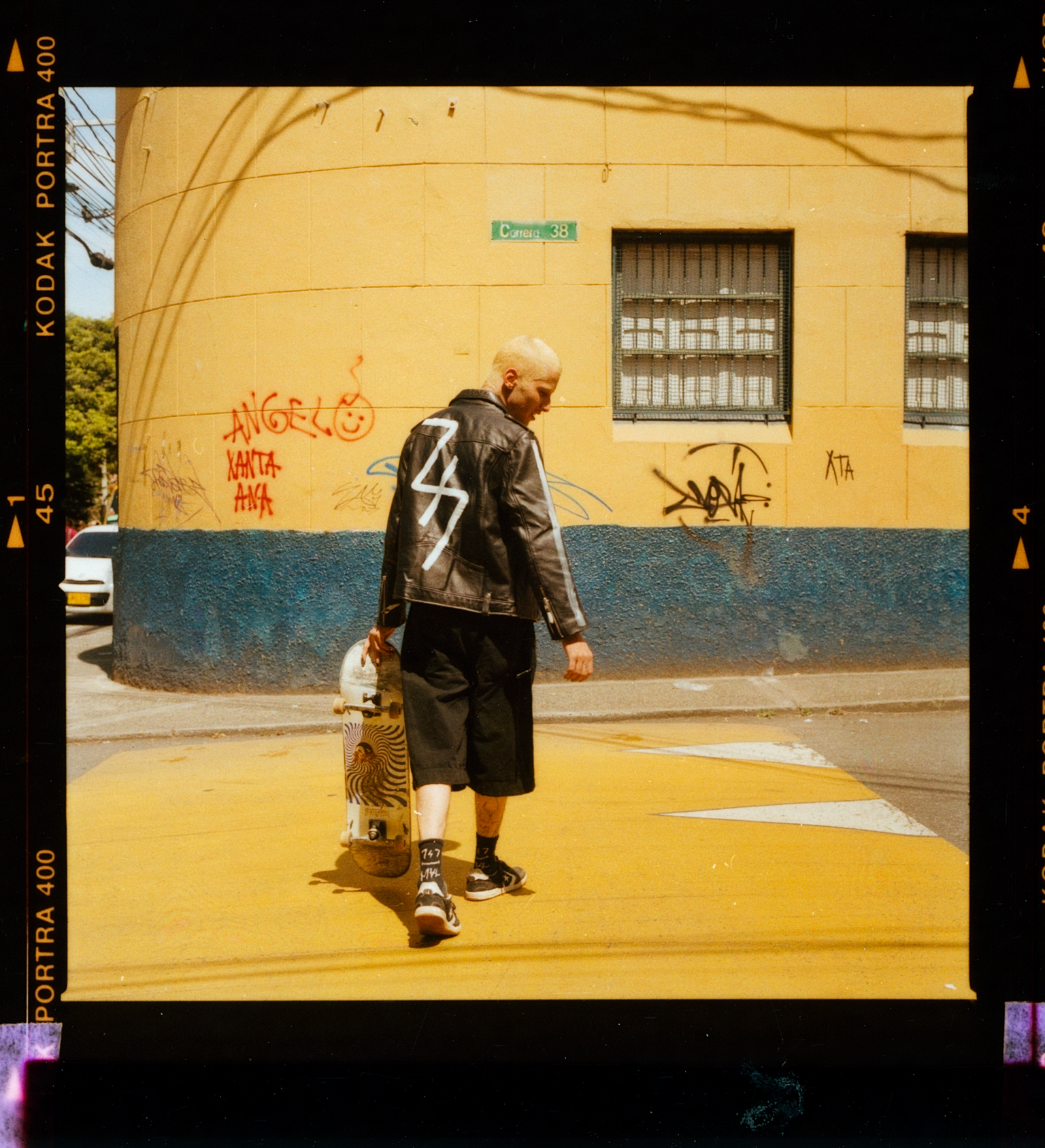Bald man in dark jacket walking with small child on yellow street, blue and yellow building with graffiti behind them.