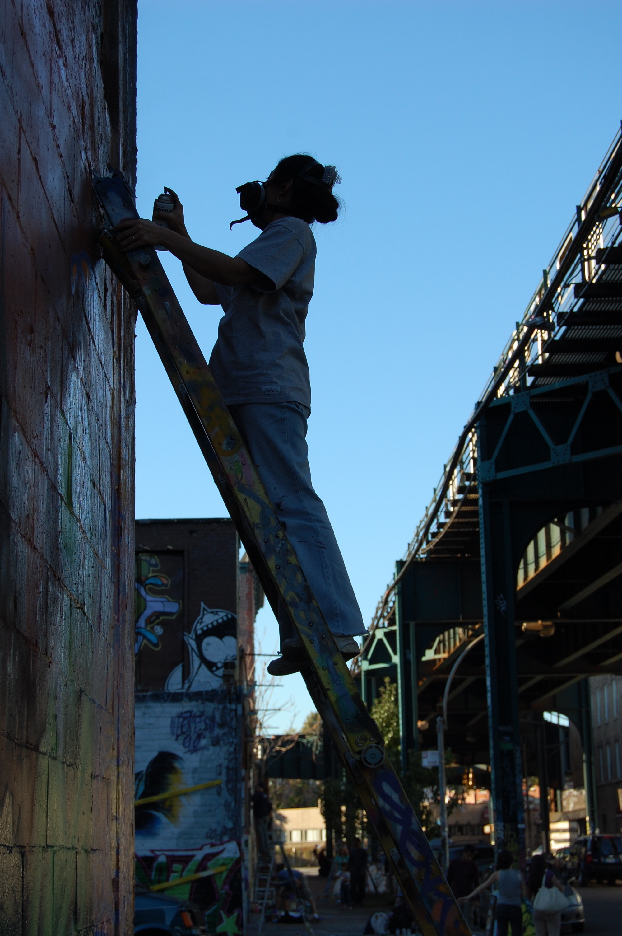 Silhouetted figure on ladder against brick wall with scaffolding visible on right side under blue sky.