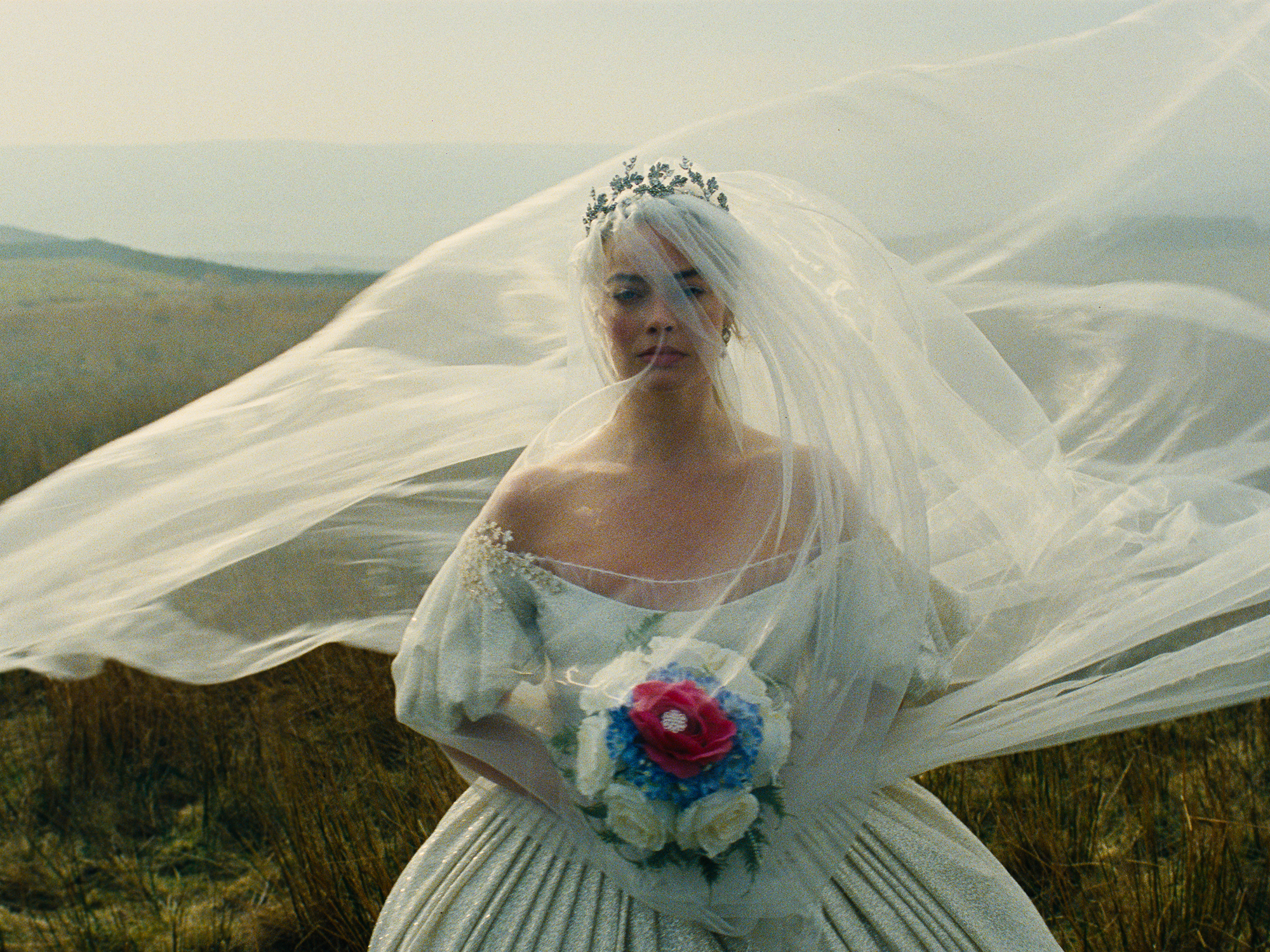 Margot Robbie as Cathy on her wedding day in Wuthering Heights, wearing a white gown and veil and carrying a red, blue and white bouquet.