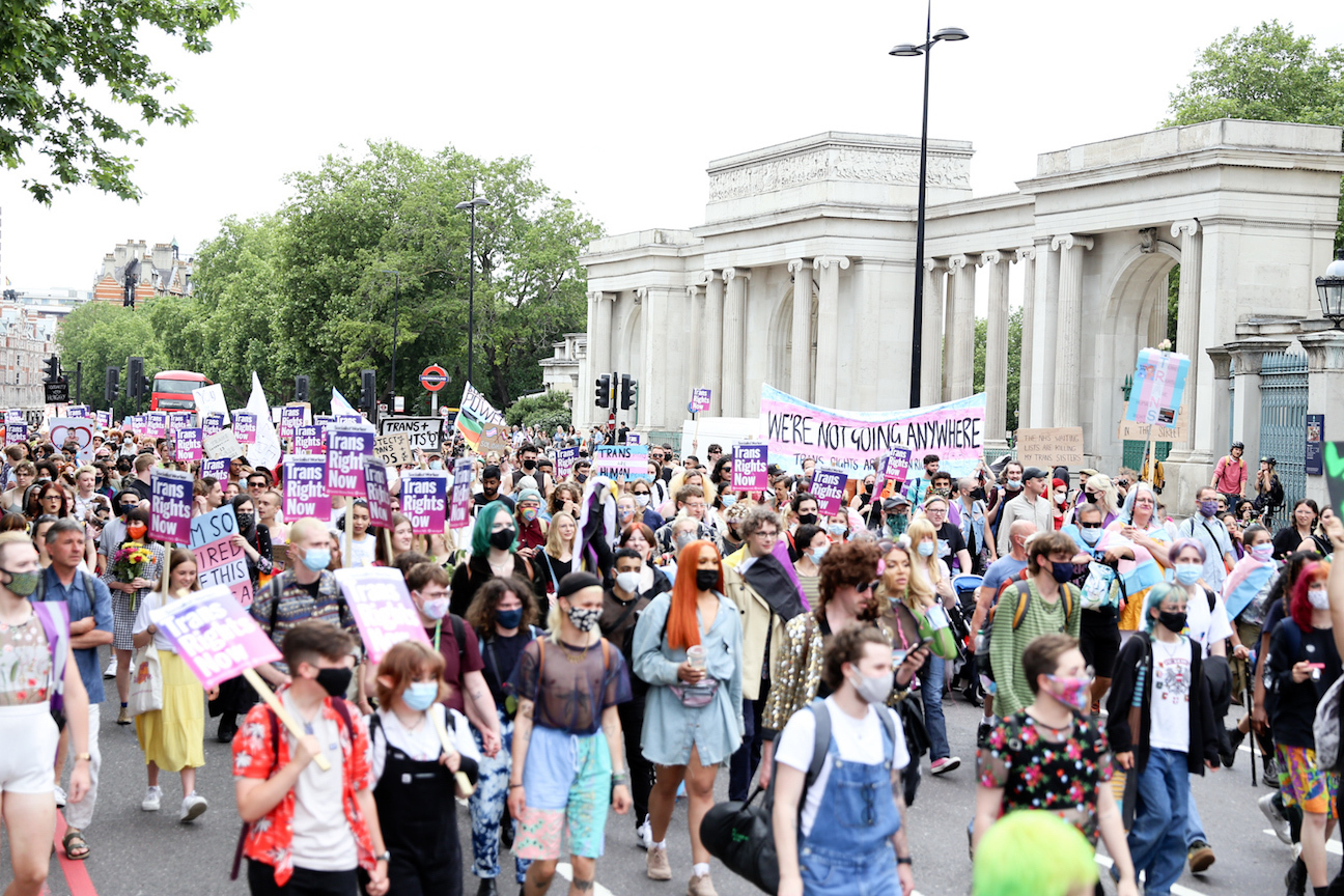 Large crowd of protesters marching with placards and banners, in front of a classical building with columns.