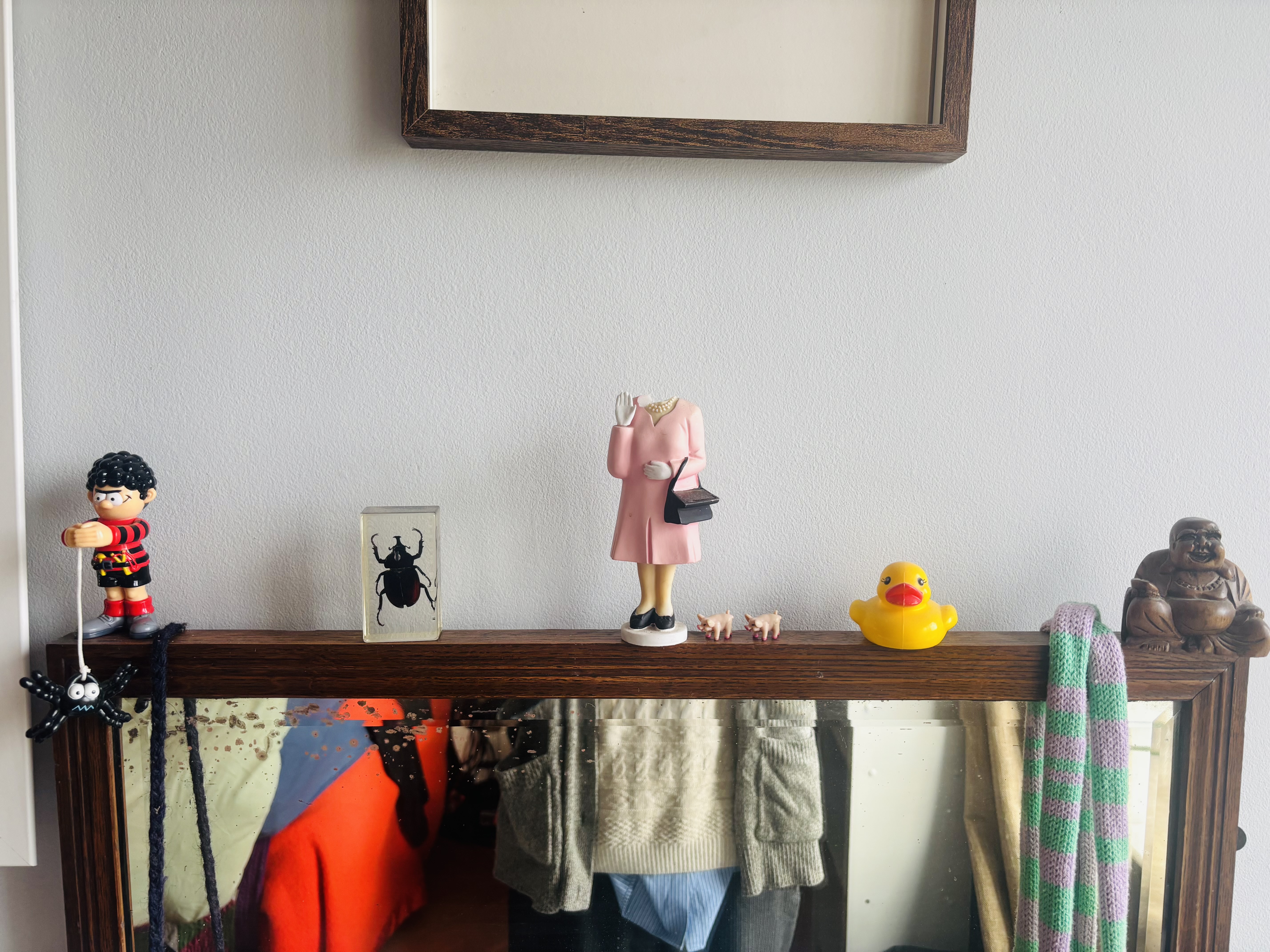 Wooden shelf with toys and ornaments: Playmobil figures, framed spider specimen, rubber duck, small ape figure, and colourful towels below.