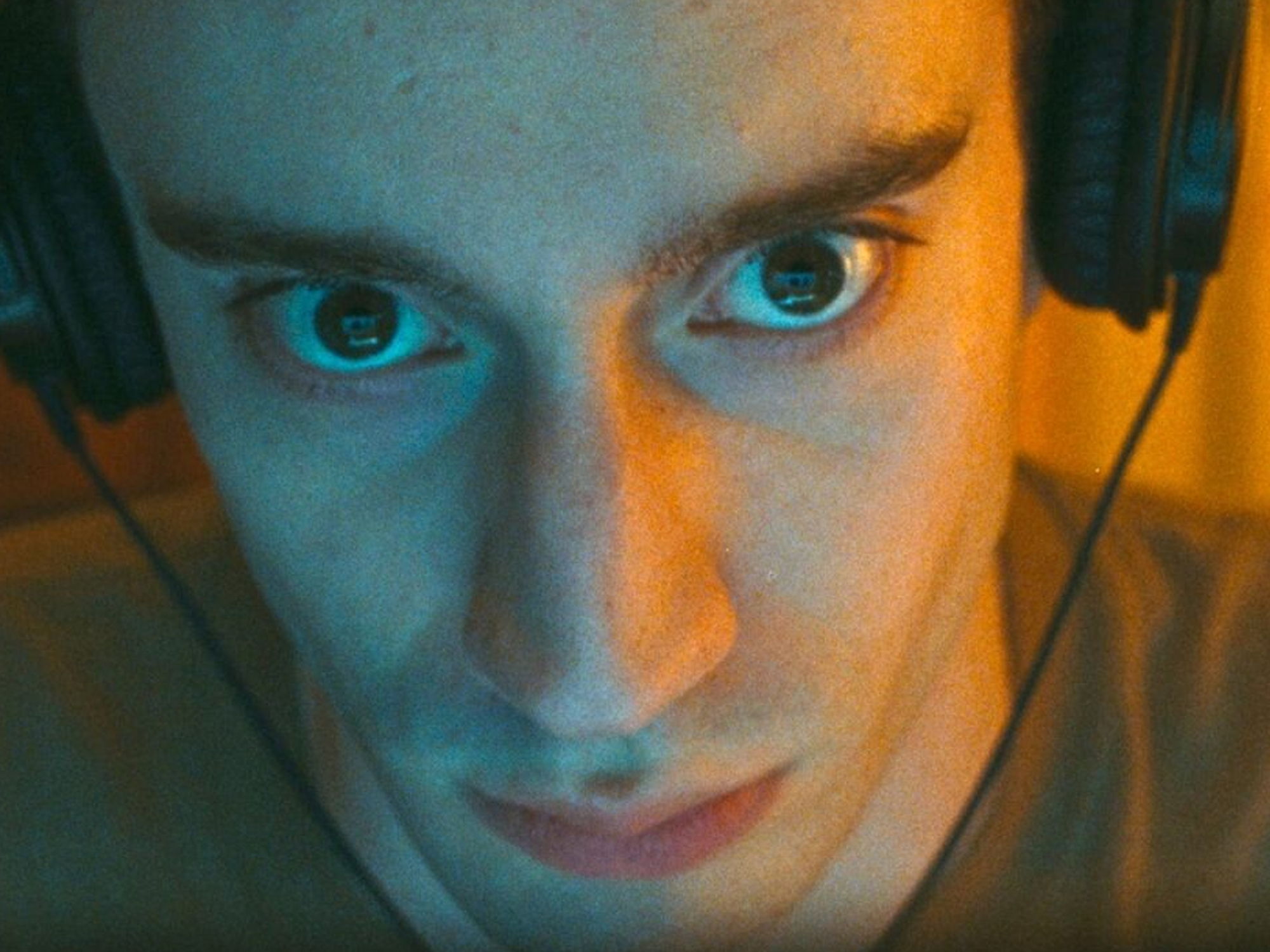 Close-up portrait of Théodore Pellerin with dramatic blue and orange lighting casting contrasting colours across face, emphasising bright blue eyes.