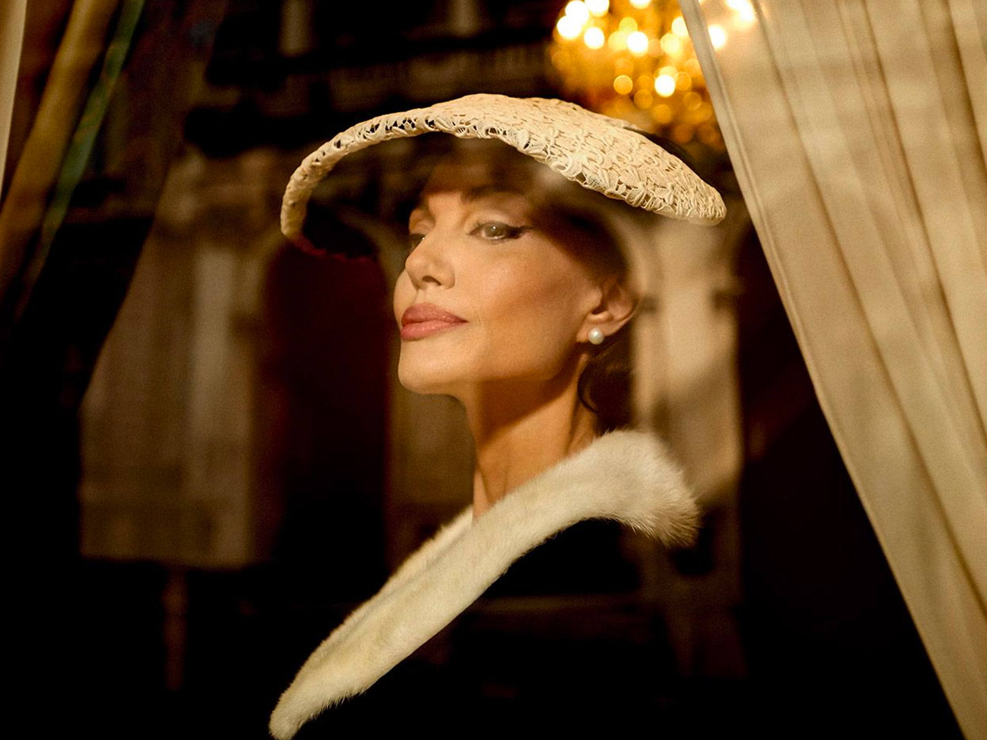 Woman wearing a wide-brimmed hat and fur-trimmed coat, gazing pensively.