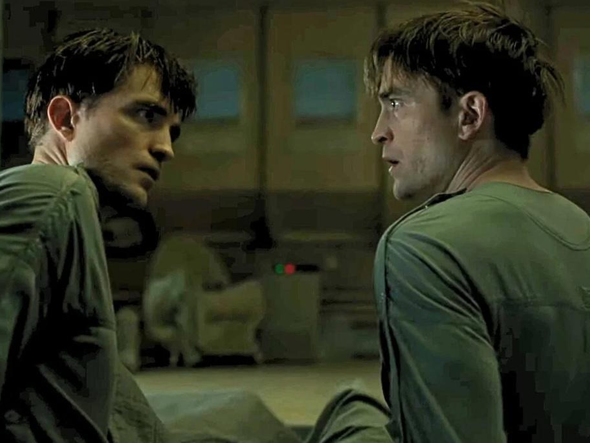 Two young men in green shirts confronting each other in a dimly lit room.