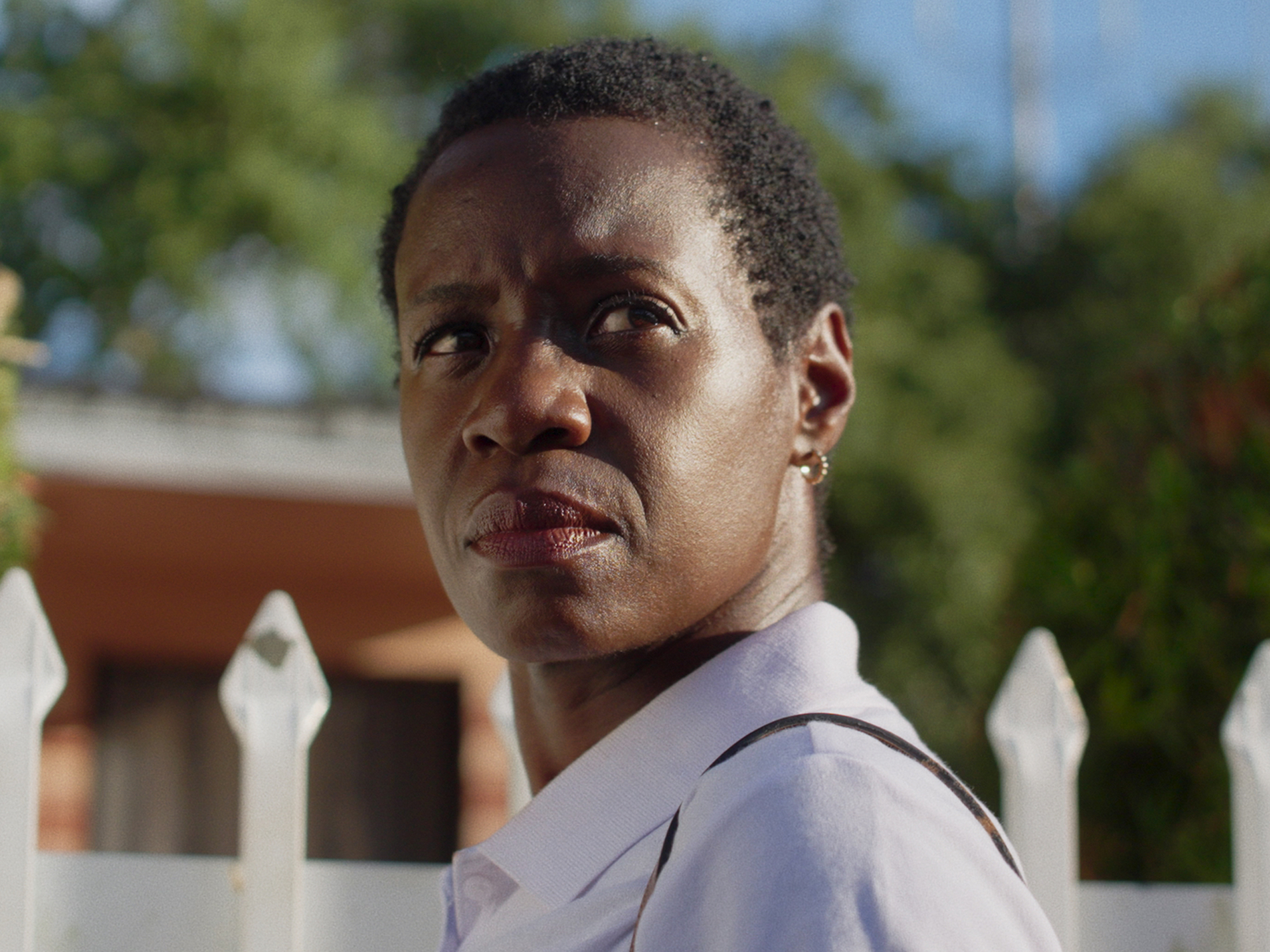 A portrait of a serious-looking Black man with short, curly hair, wearing a light-coloured shirt against a background of greenery.