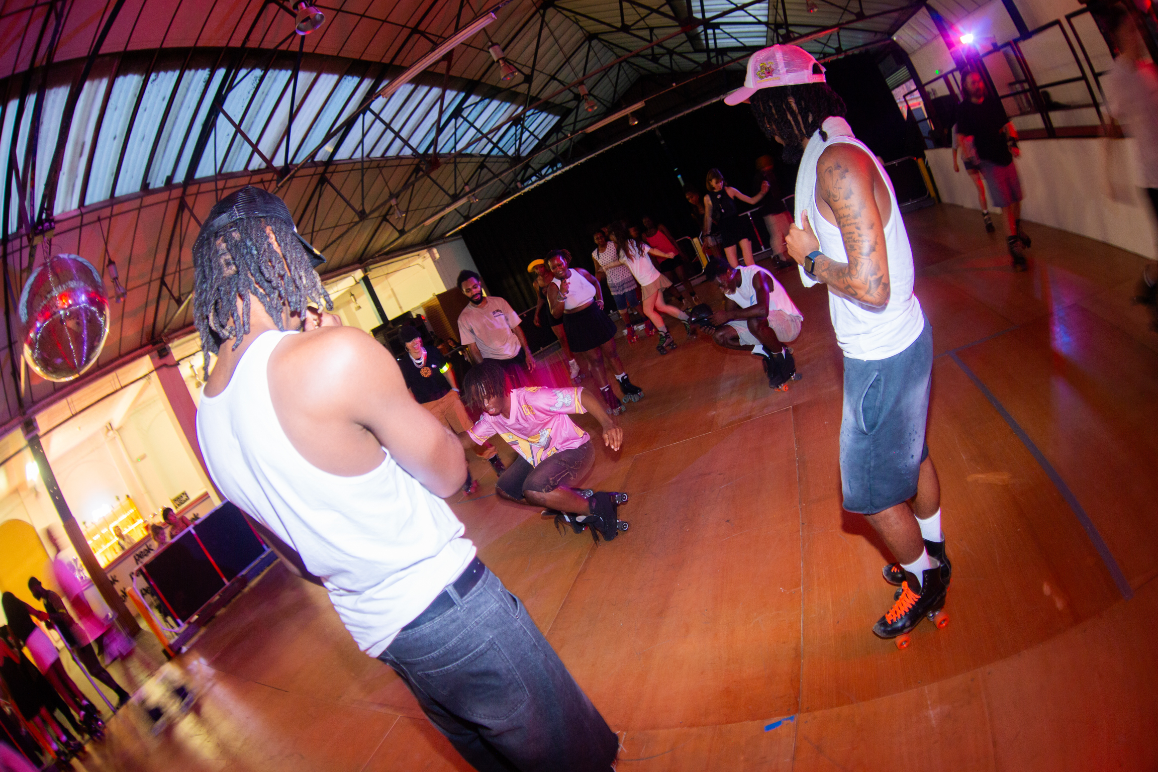 Wide-angle view of people dancing on polished floor under arched metal ceiling with warm lighting and purple accents.