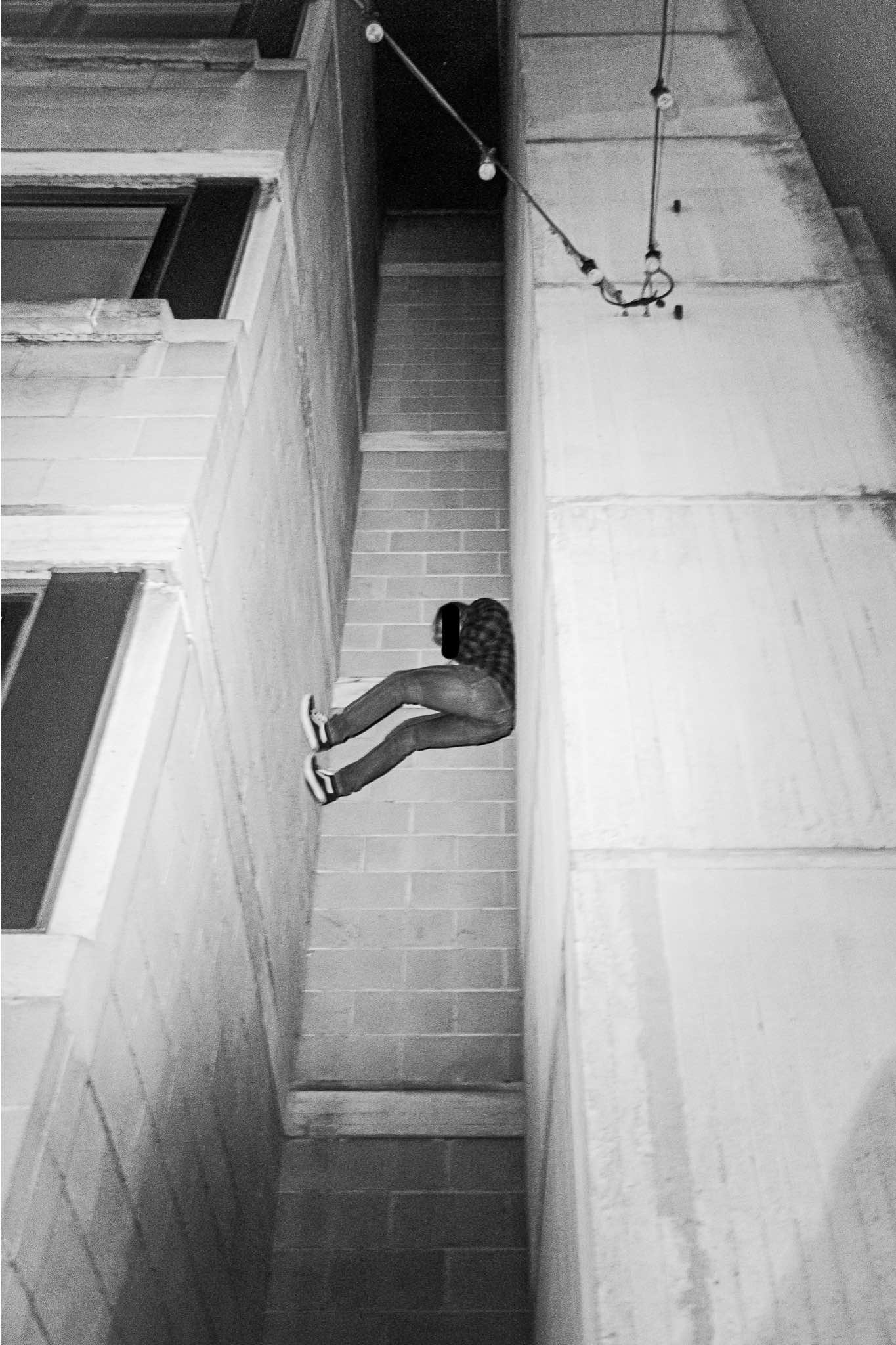 Black and white image showing person sitting on concrete steps between angular walls, with handrail visible above.