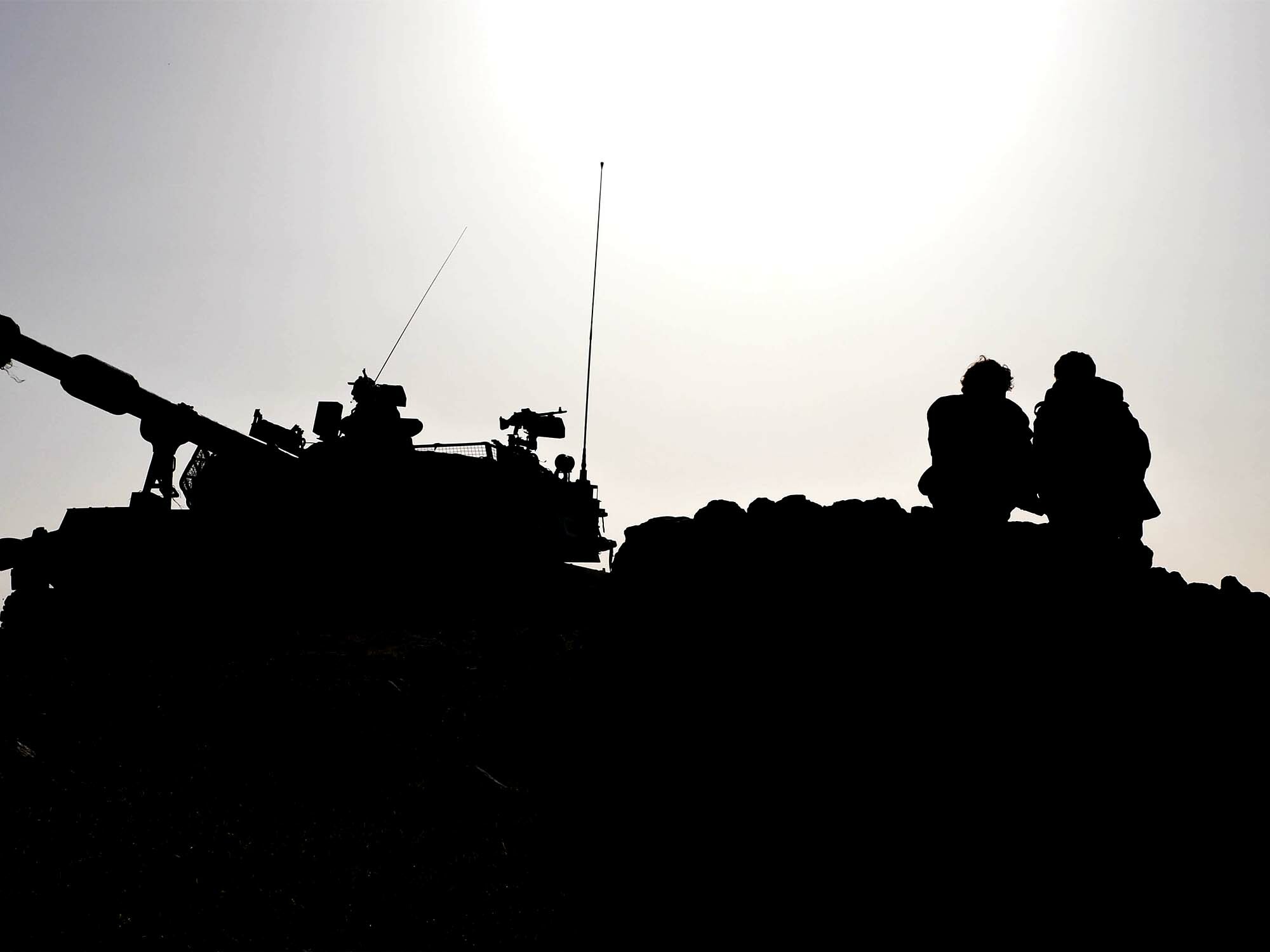 Silhouetted armoured military vehicle on rocky terrain, figures in foreground
