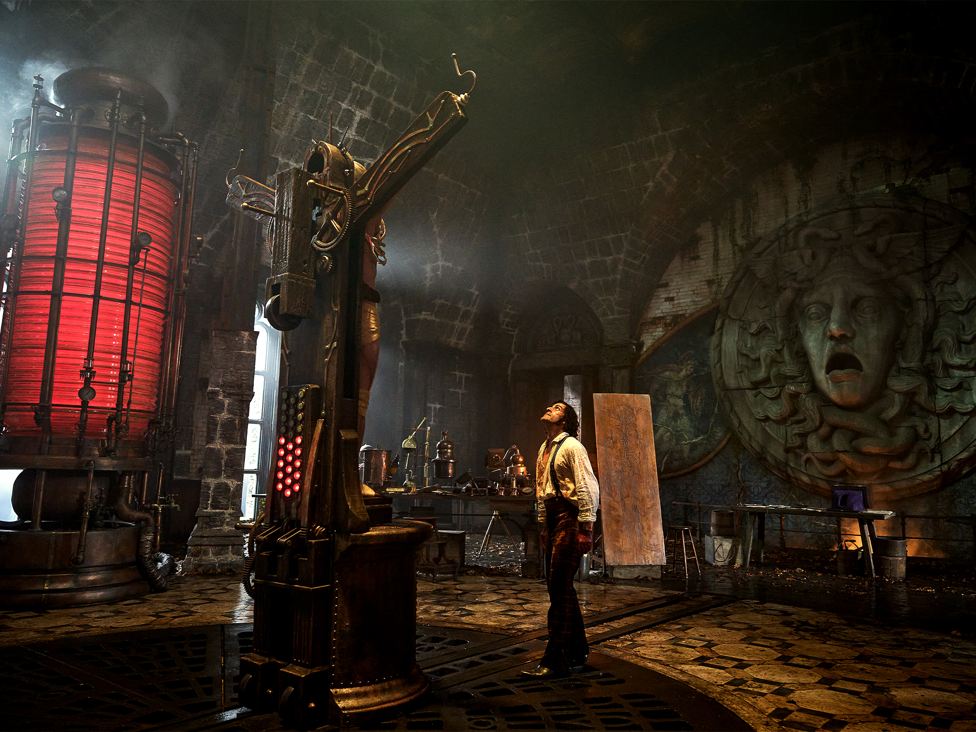 Dark underground chamber with red glowing cylindrical structure, bronze machinery, stone carvings on walls, and figure standing on tiled floor.