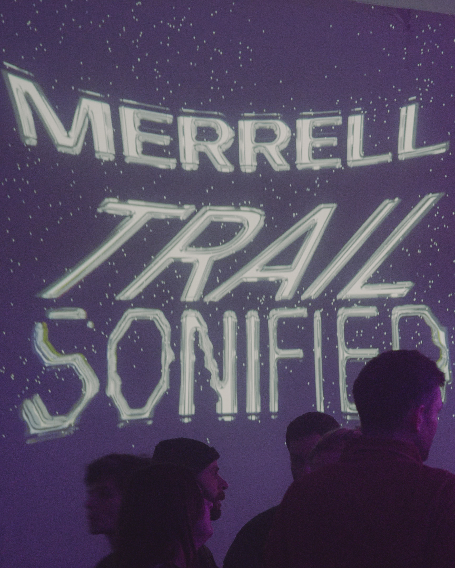 Purple starry background with white text reading "MERRELL TRAIL SONIFIER". Dark silhouettes of people's heads visible at bottom.