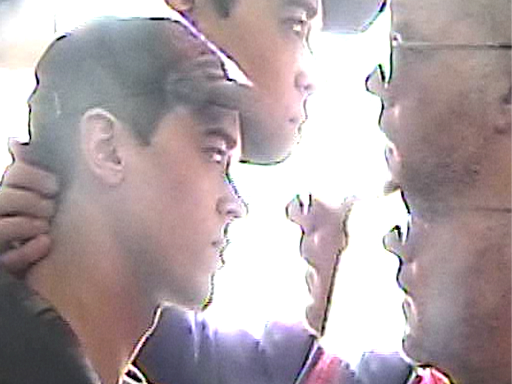 Two men in profile view looking at cracked mirror, reflections fragmented by diagonal crack lines across glass surface.