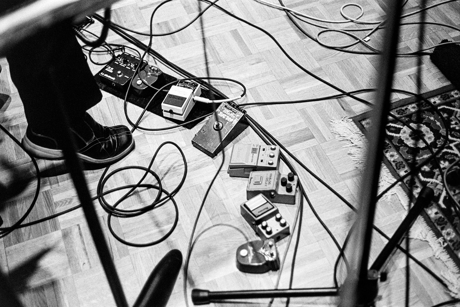 Black and white image showing tangled cables and electronic equipment on a floor, viewed from above with shadows cast across the scene.