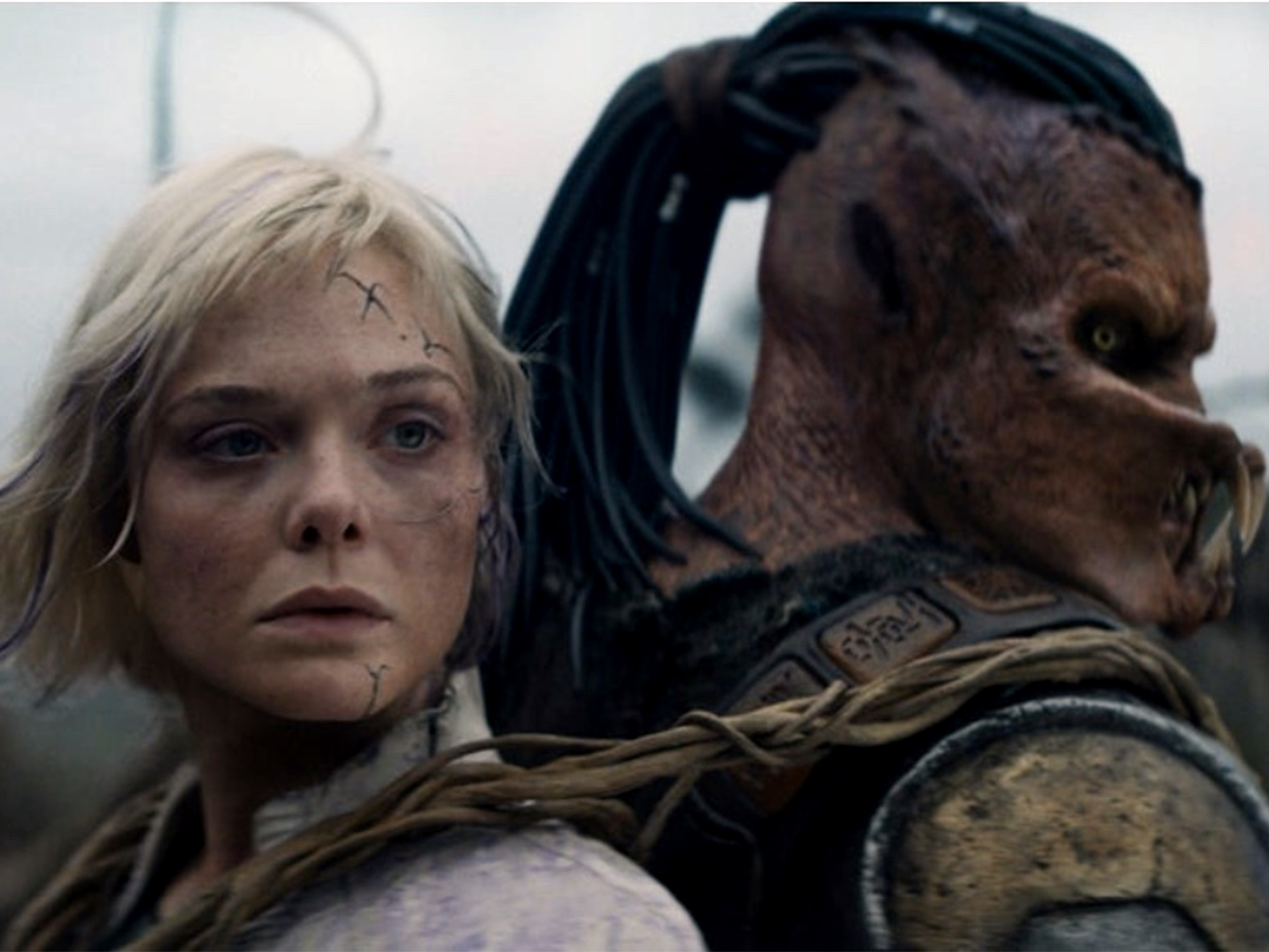 Blonde woman with facial wounds beside alien creature with dark dreadlocks and mottled brown skin in military gear.