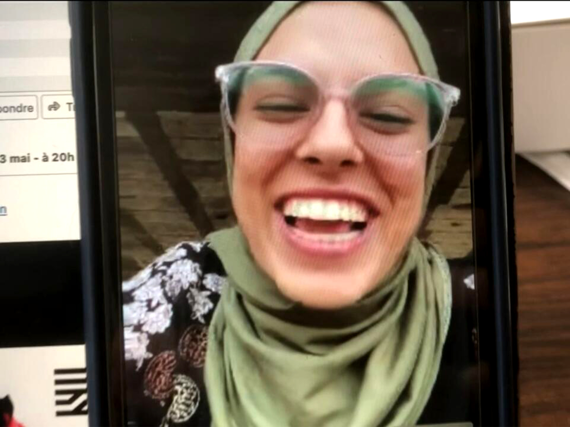 Woman laughing wearing green headscarf and glasses on a smartphone screen.