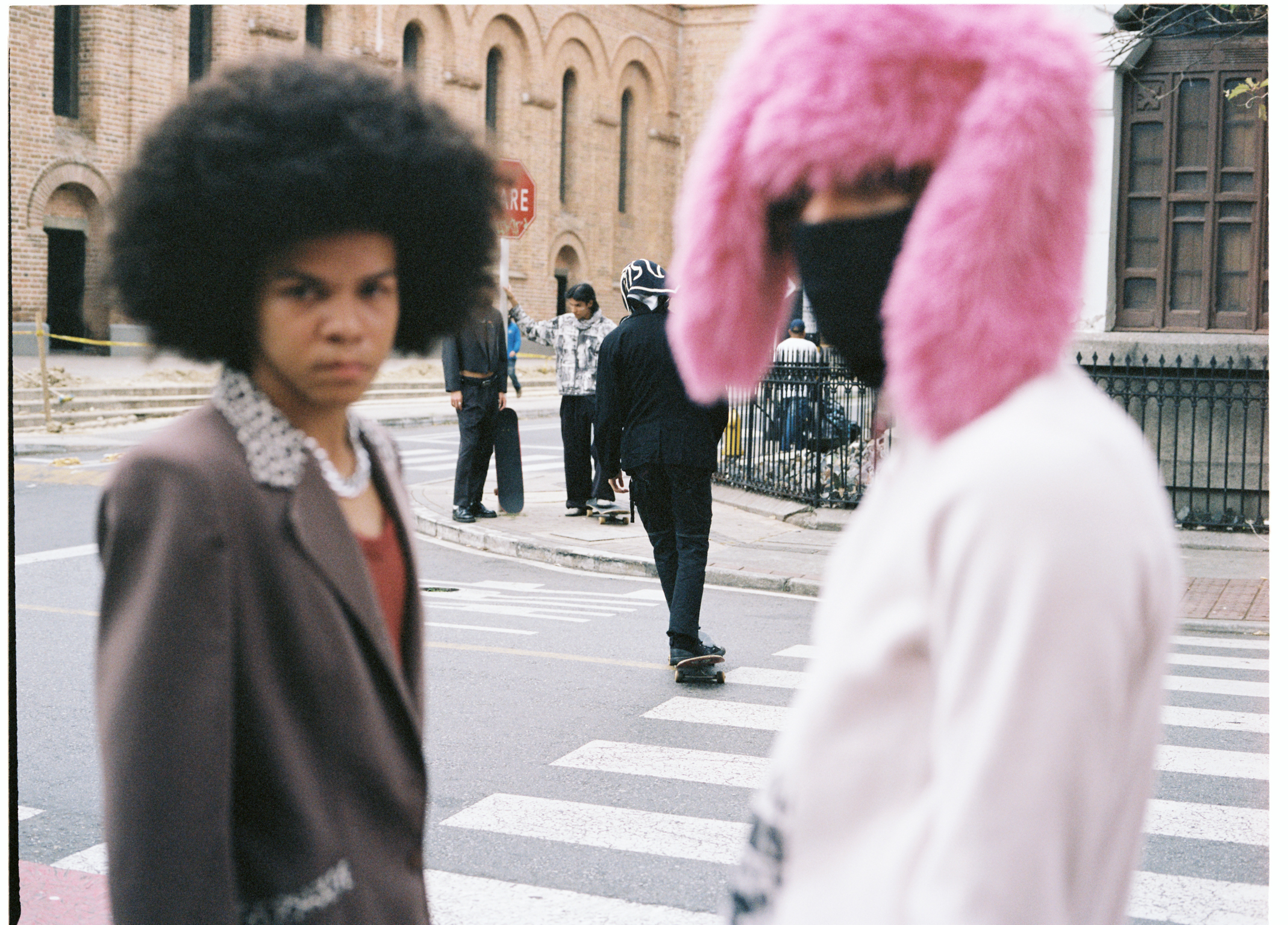 Woman with dark afro hair in grey coat and person with bright pink hair in white top on street with historic stone buildings