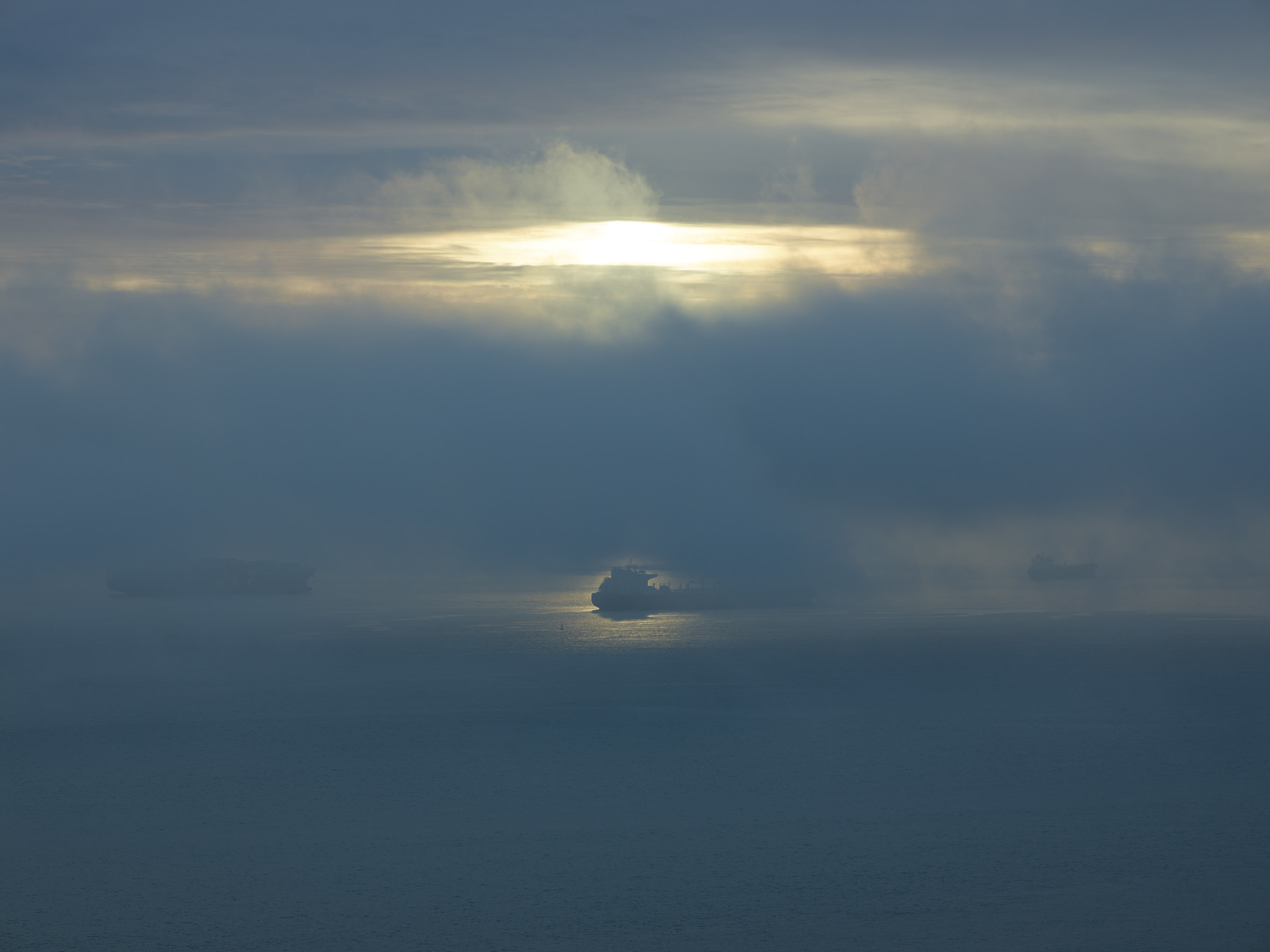 Cloudy sky with bright white and yellow light breaking through grey and blue cloud layers in horizontal bands.