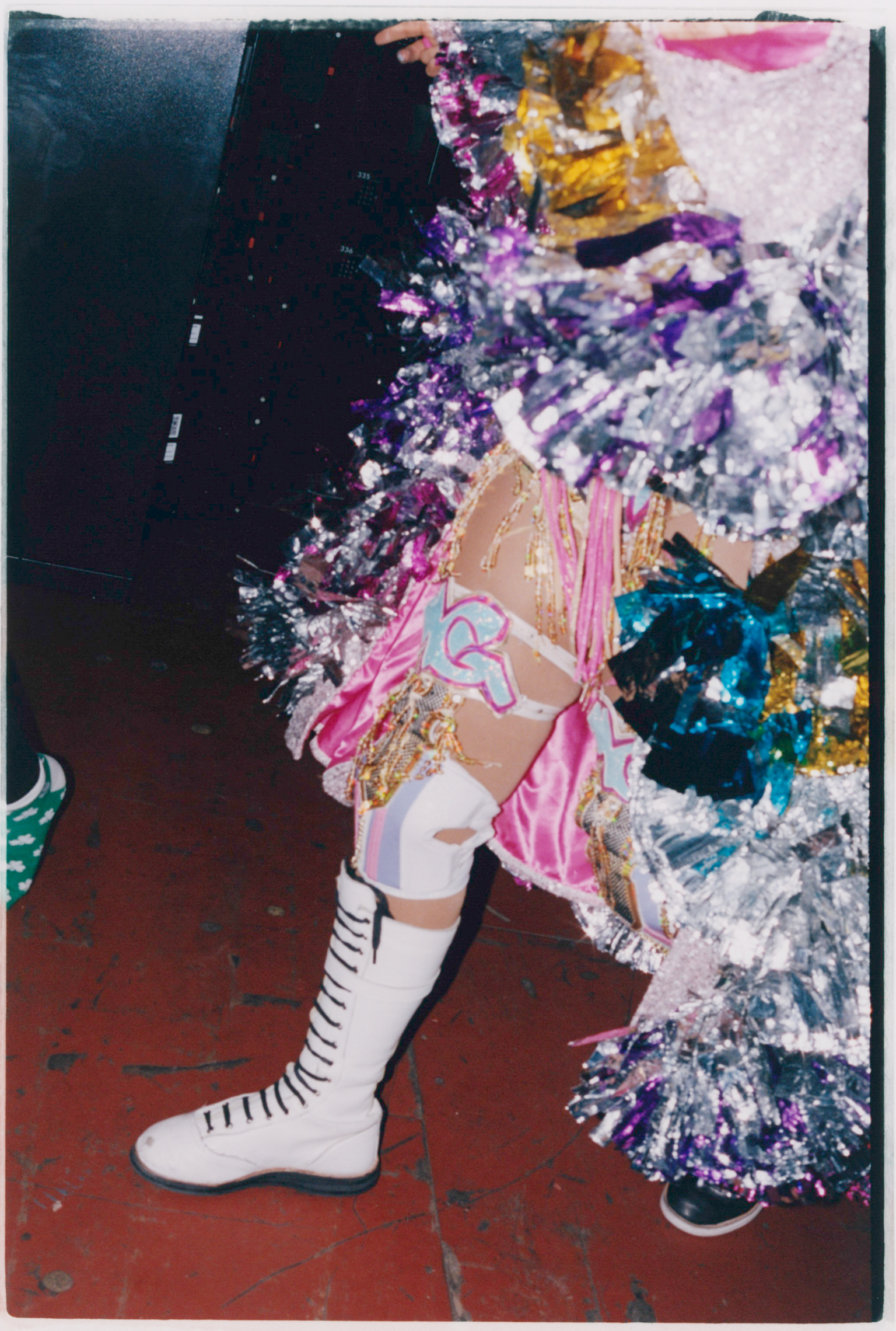 Mixed media collage with pink, purple, and teal elements scattered across white and dark sections. White boot with black stripes visible at bottom.