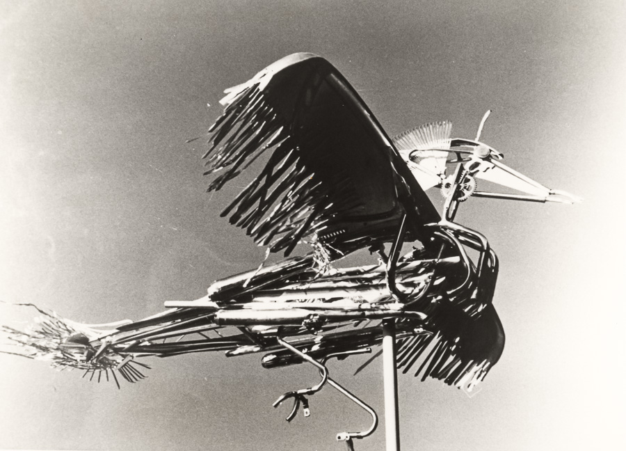 Black ink brush strokes forming abstract bird-like shape with angular wings and curved lines on grey-white background.