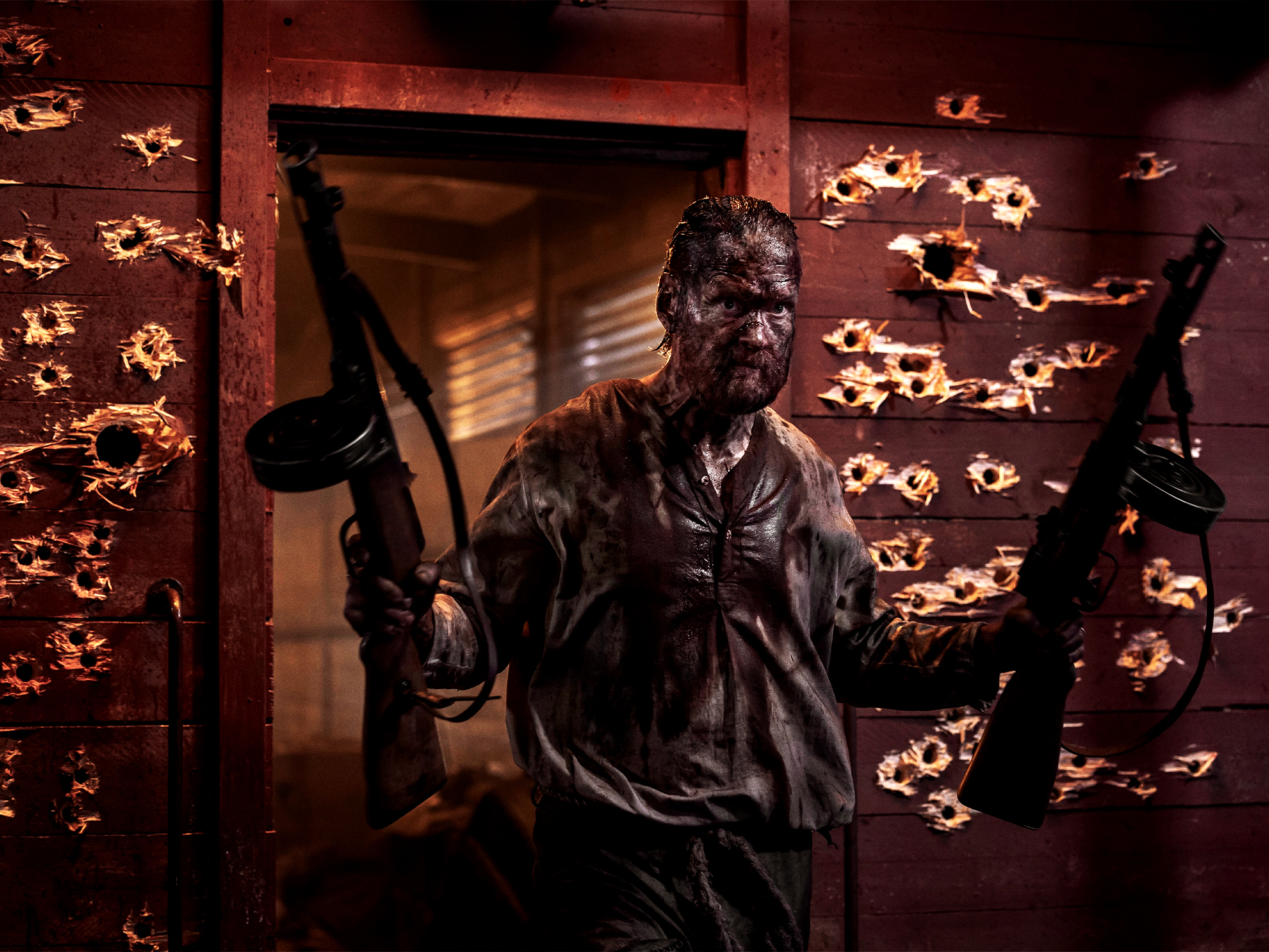 Person in dark clothing holding rifle, standing in doorway with orange flames and smoke filling background.