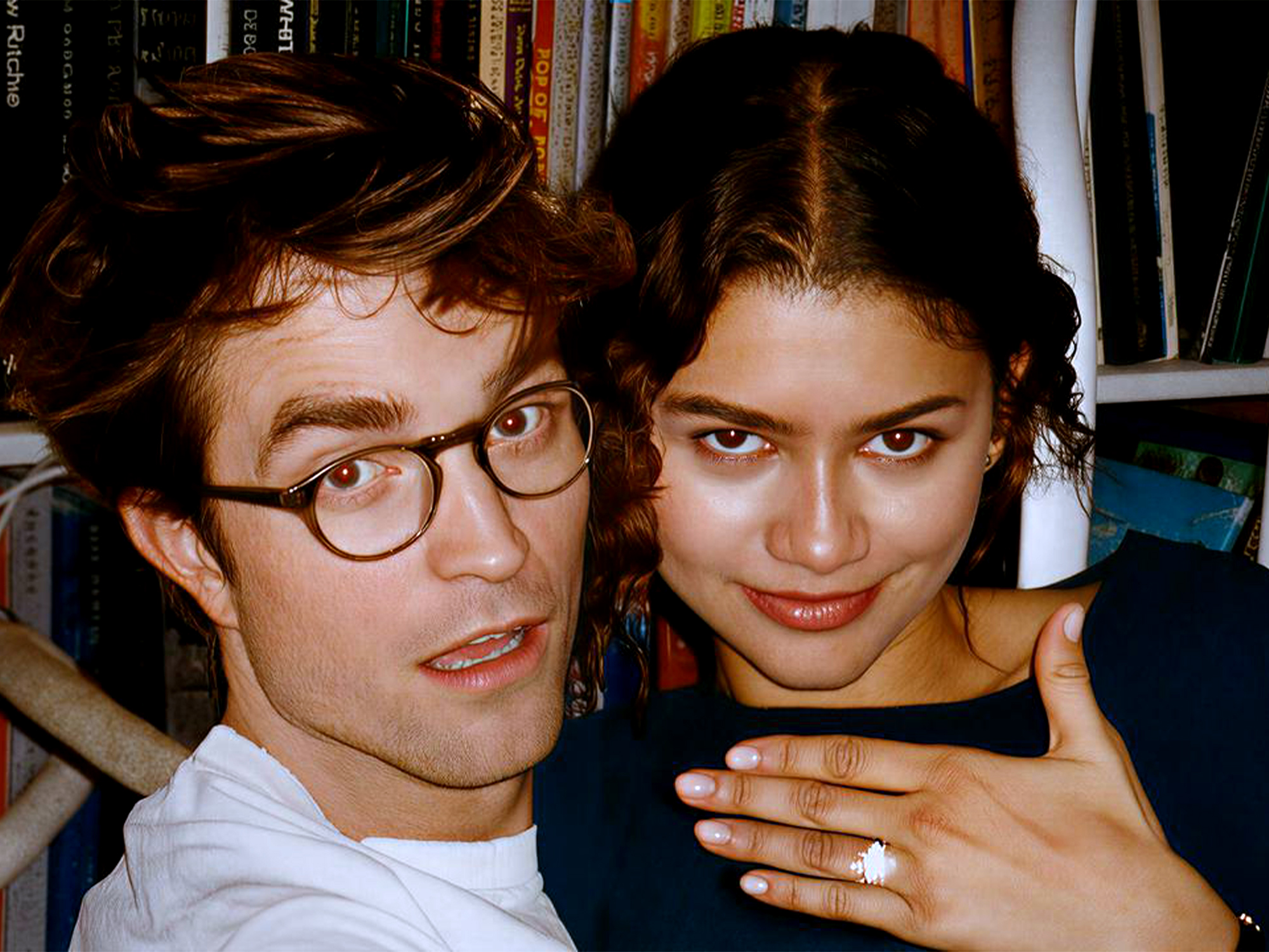 Man with glasses and woman smiling at camera in front of bookshelf filled with colourful books.
