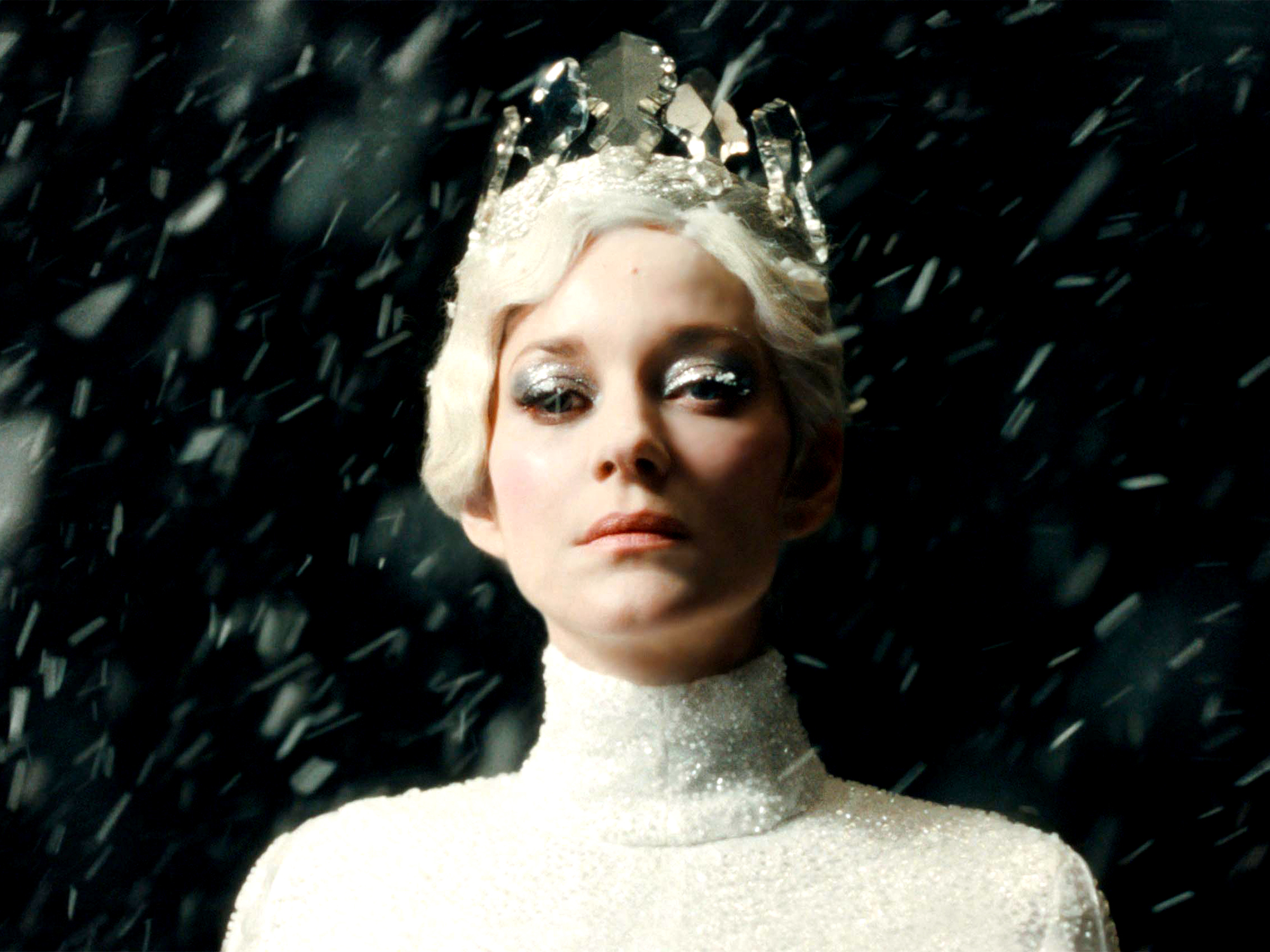 Woman with platinum blonde hair and silver crown against dark background with diagonal white streaks resembling falling snow.