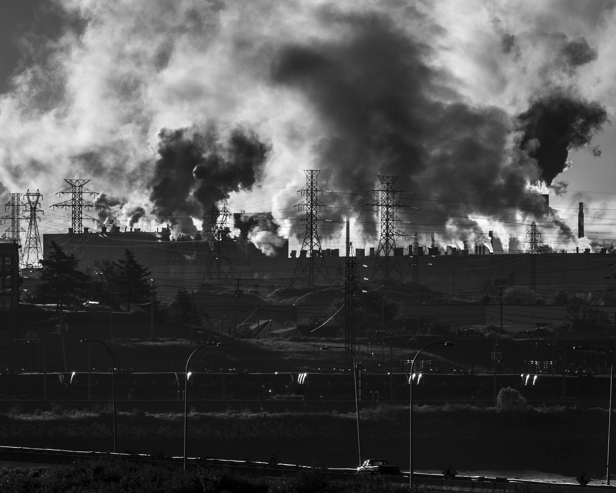 Sprawling industrial landscape with billowing smoke and chimneys against a dark sky.