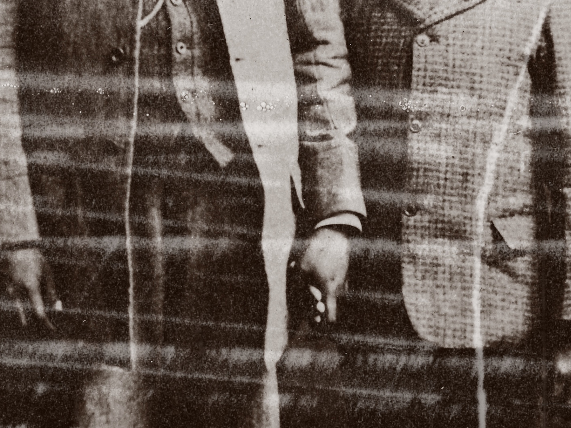 Black and white image showing person's torso and hands holding white ribbon or fabric against striped background.