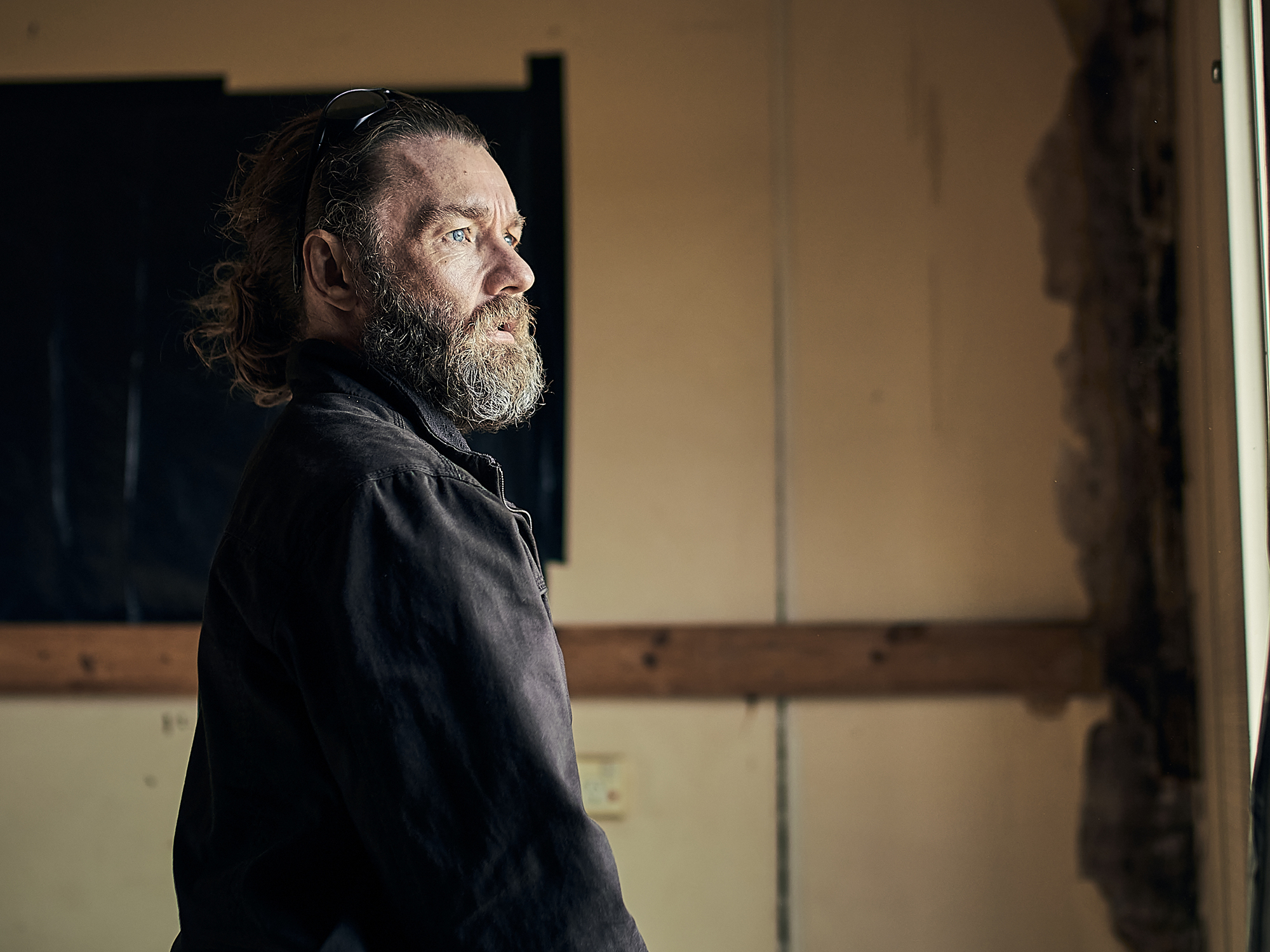Close-up of a bearded man in a dark coat, looking pensive and deep in thought.