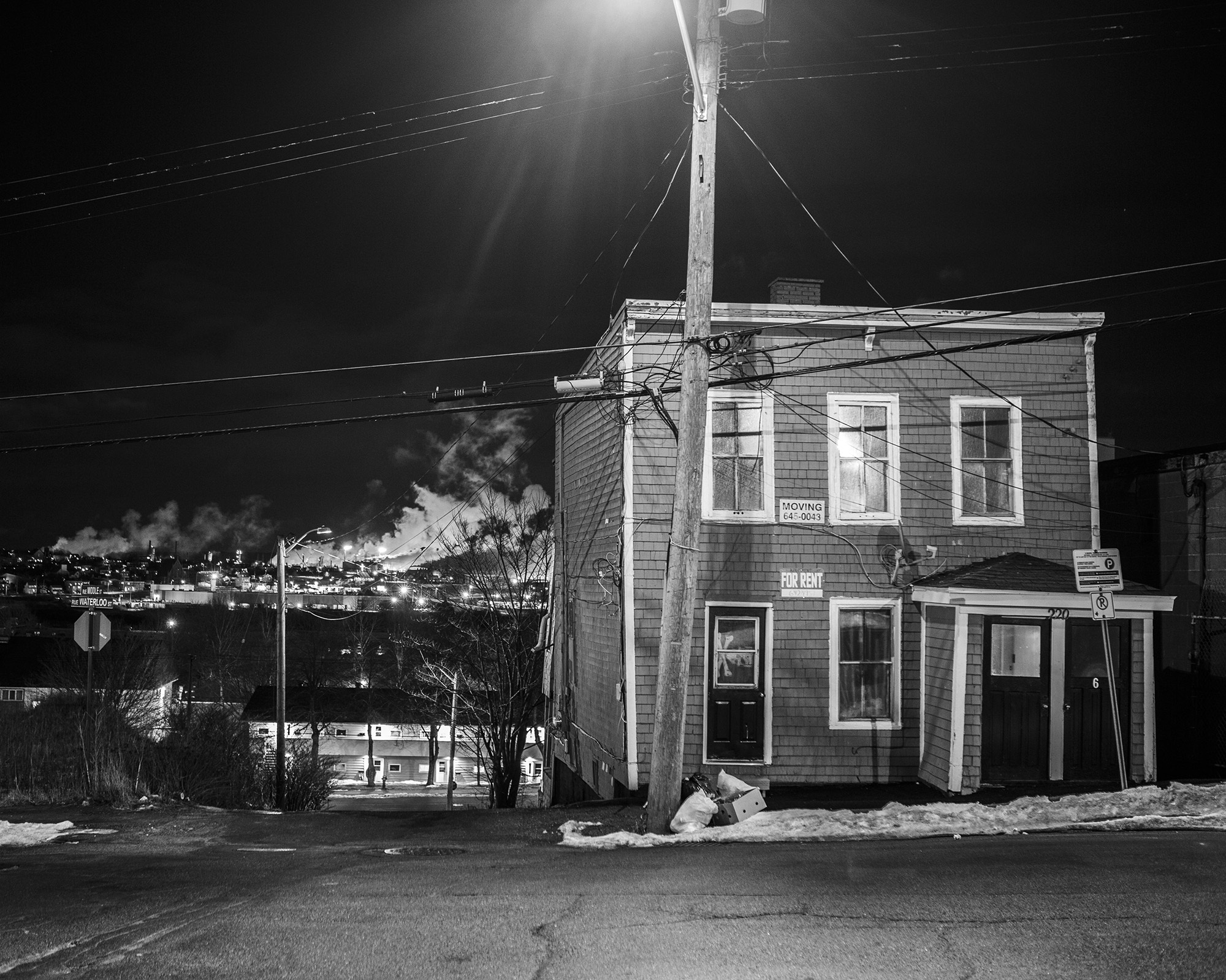 Dimly lit 2-storey wooden building at night, surrounded by electric lights and utility poles.