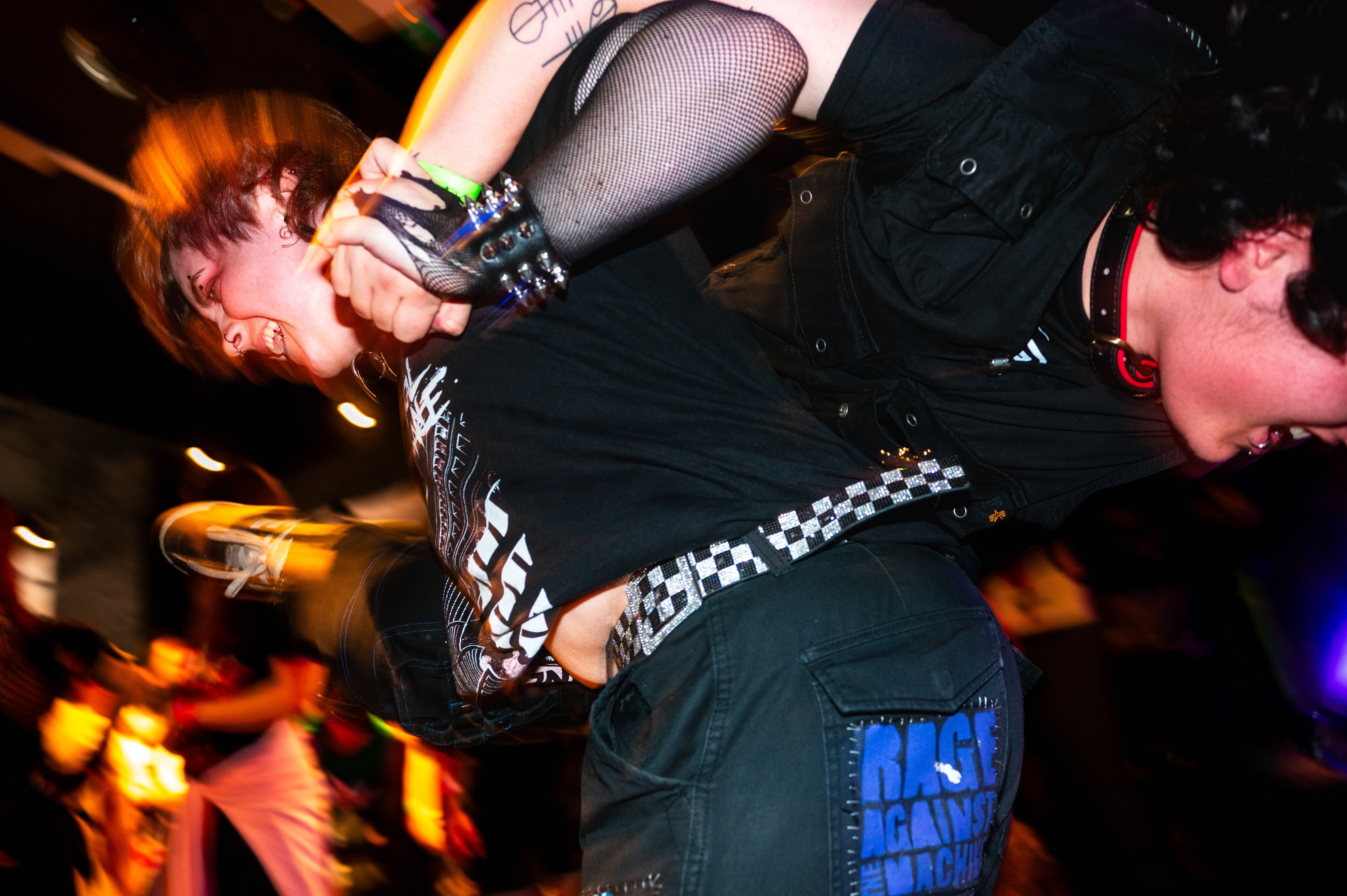 Two people performing on stage with guitars in dim lighting with orange and blue tones, motion blur effects visible.