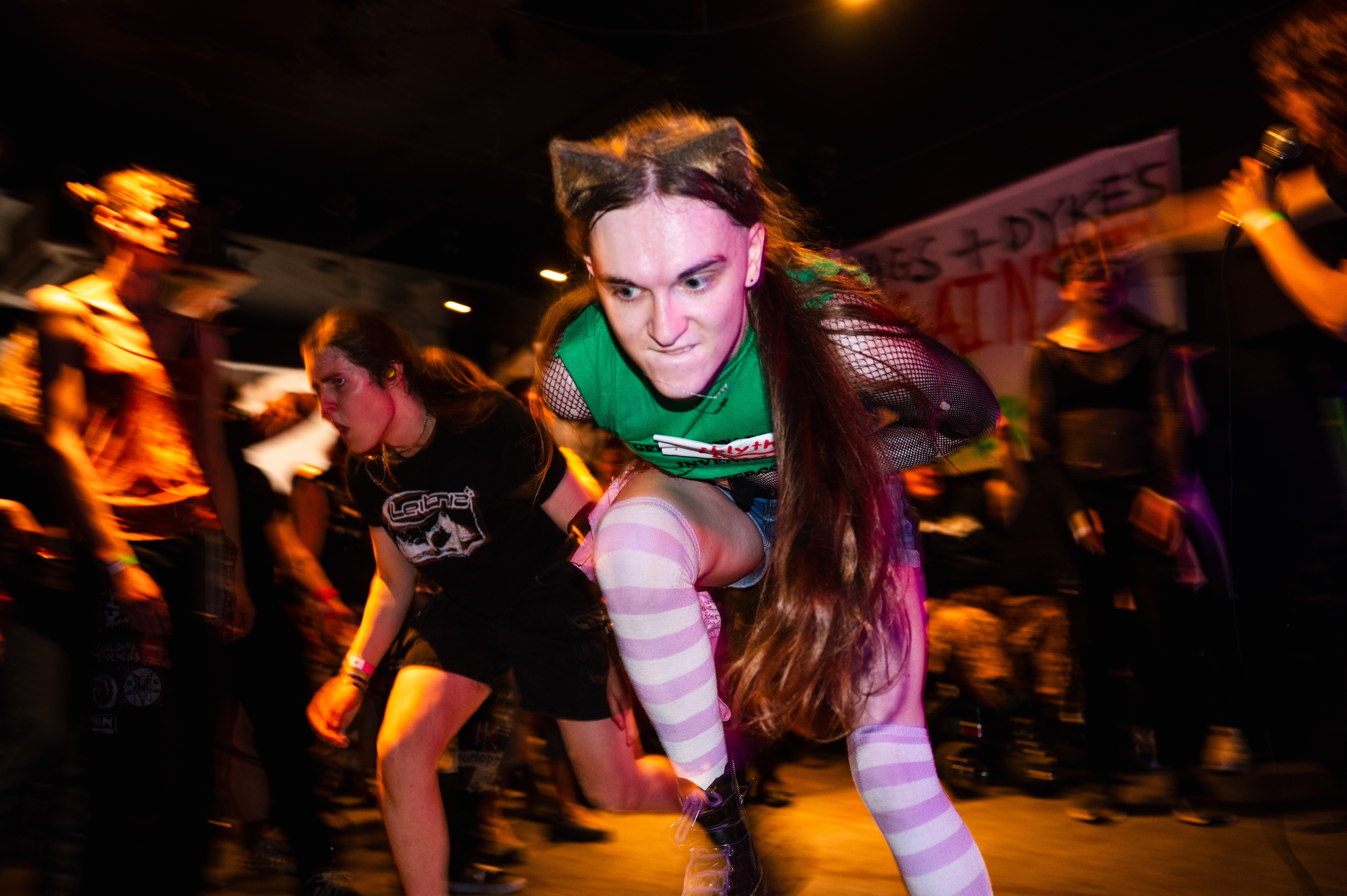 Woman in green top dancing at crowded nighttime event with motion blur and orange lighting effects