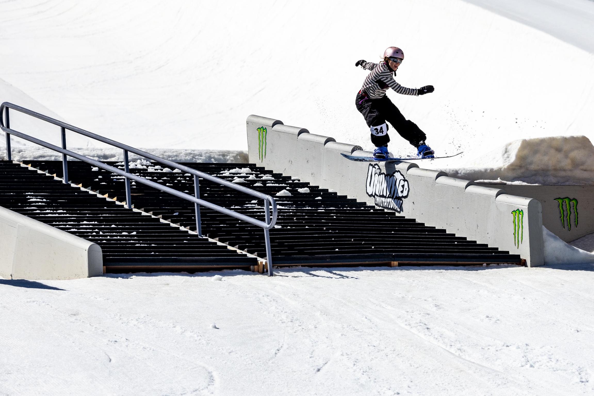Snowboarder grinding on black metal staircase handrail with white snow surrounding the structure.
