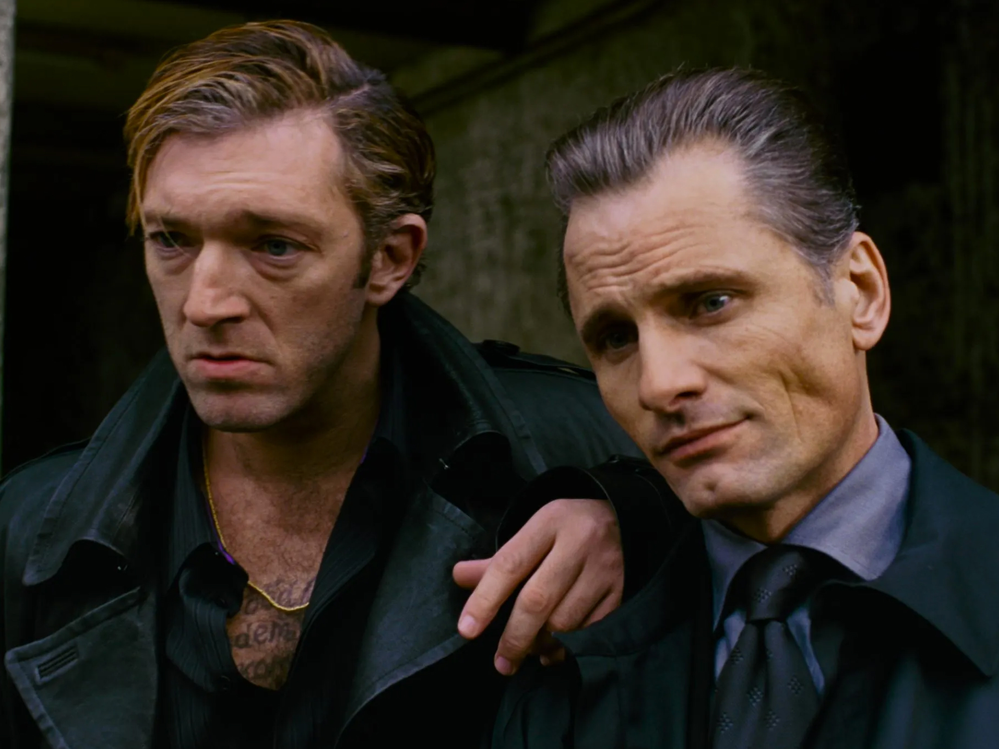 Two men wearing dark jackets and ties in a sombre expression.