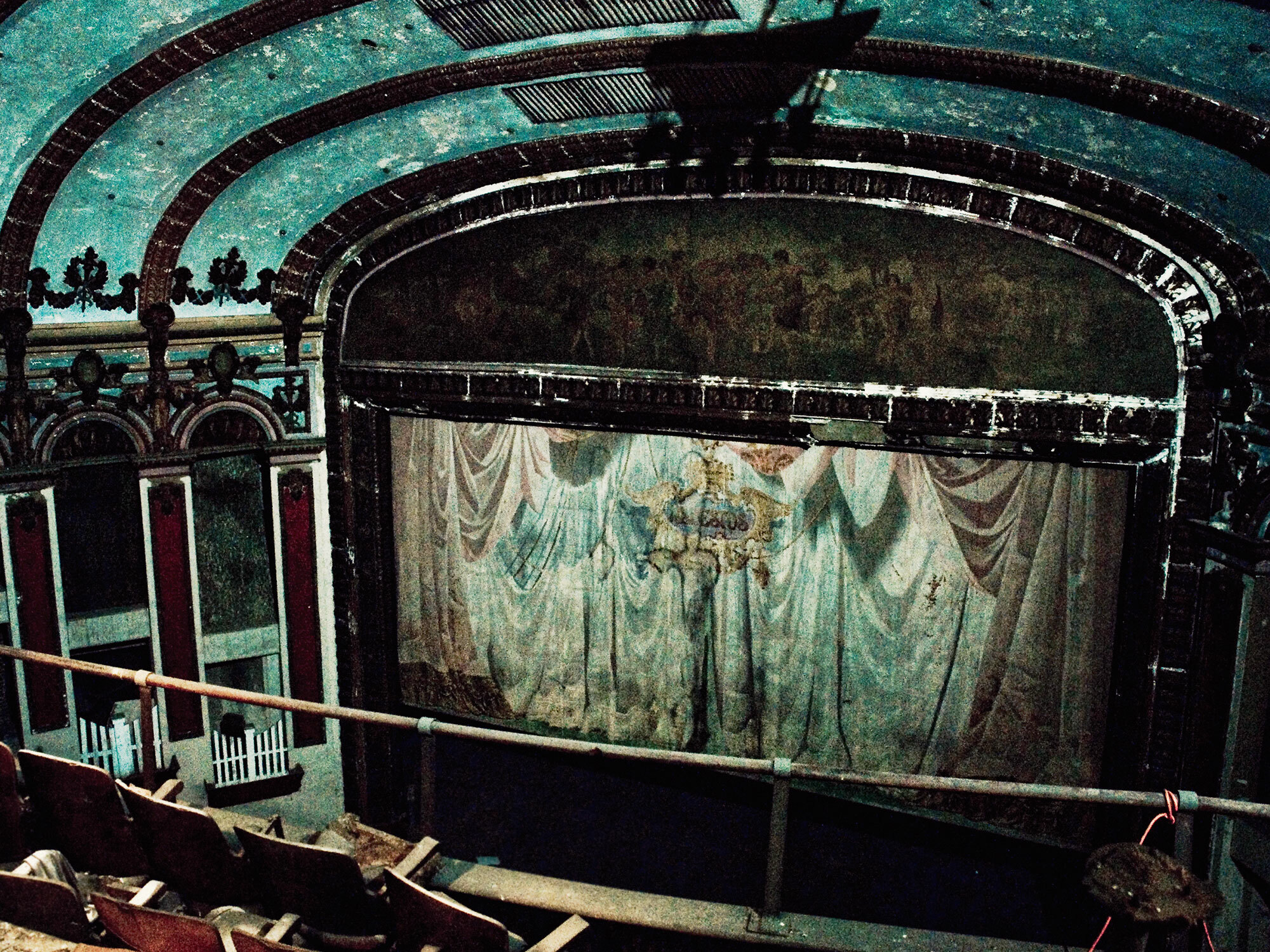 Green and black ornate interior of an old theatre with a large stage curtain.