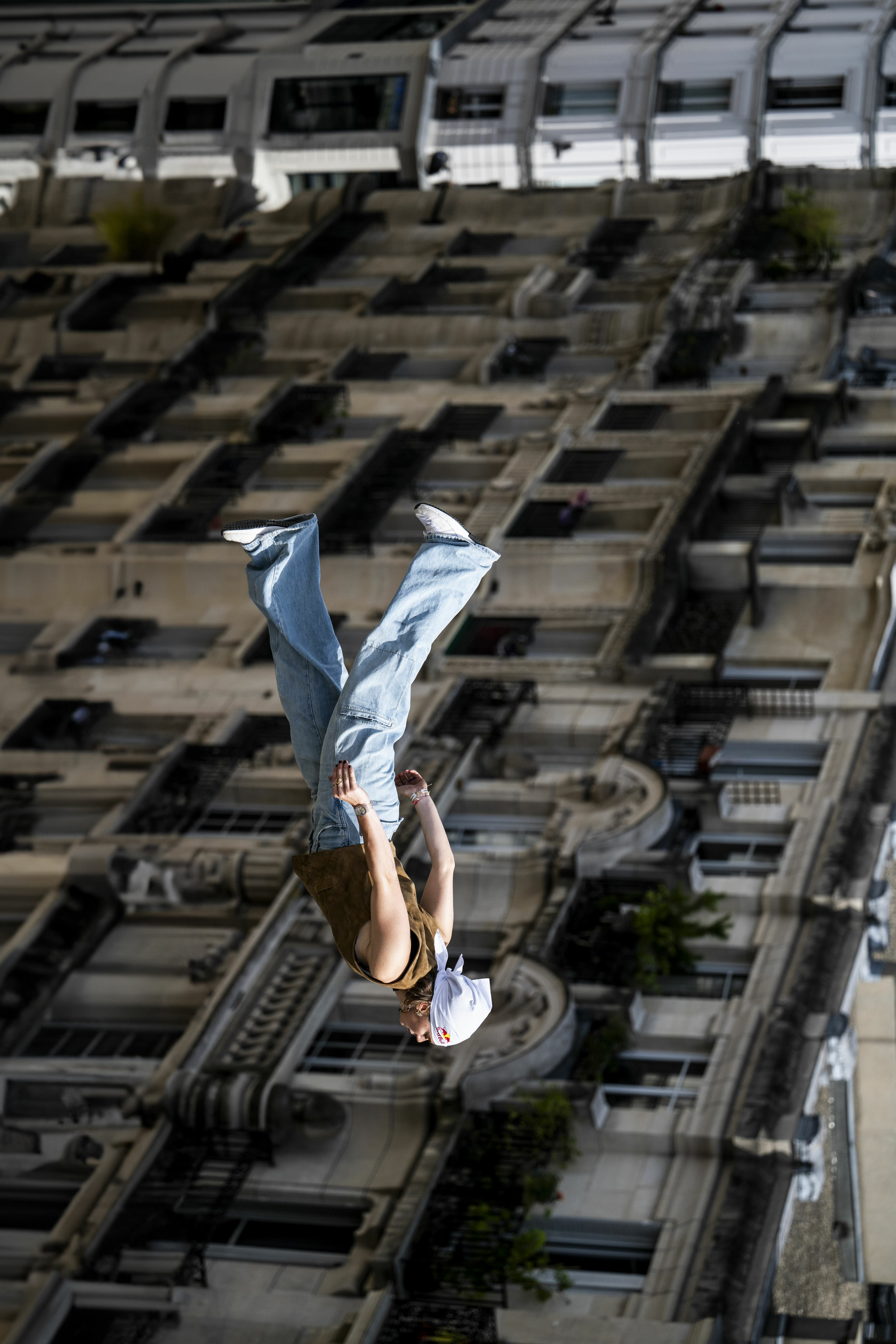 Person in light blue clothing doing handstand with urban cityscape and buildings visible far below in background.