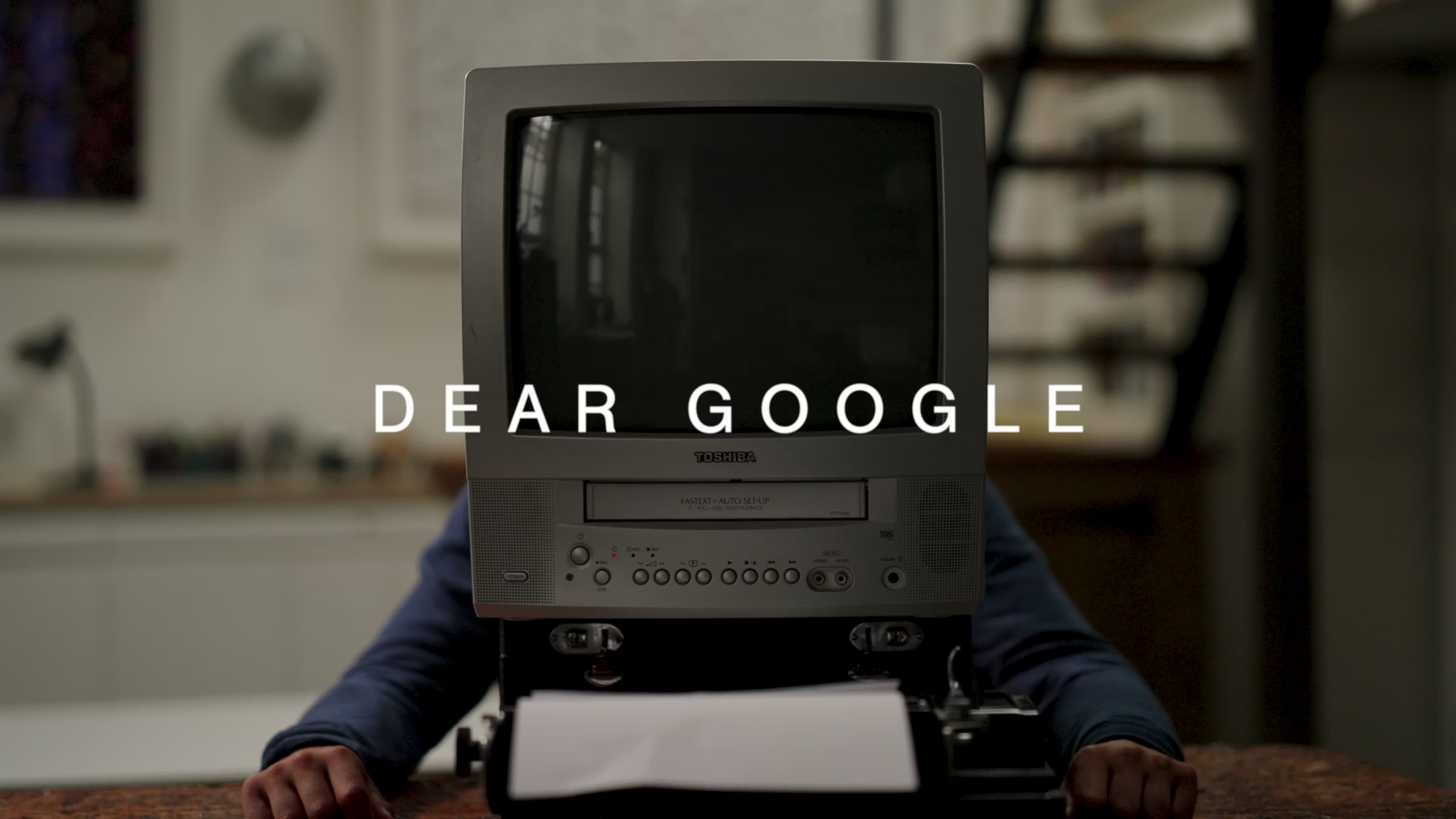 Person in navy jumper sits at desk with vintage grey CRT monitor covering their head, white text "DEAR GOOGLE" overlaid on screen.