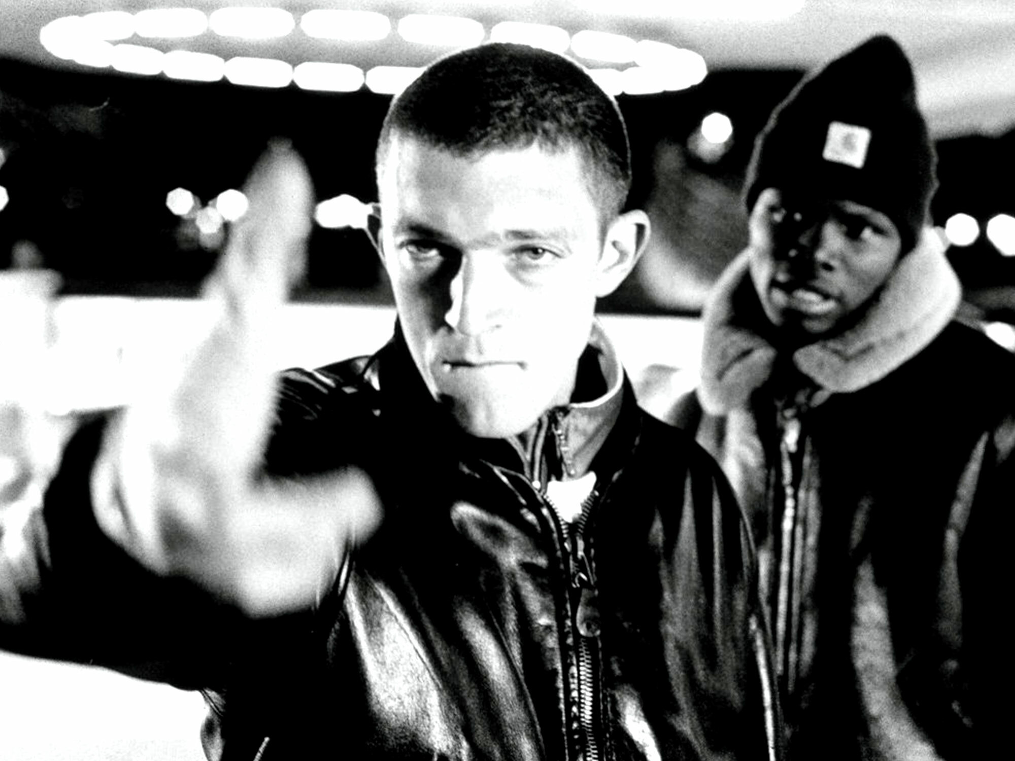 Two young men in leather jackets, one gesturing towards the camera, black and white image.