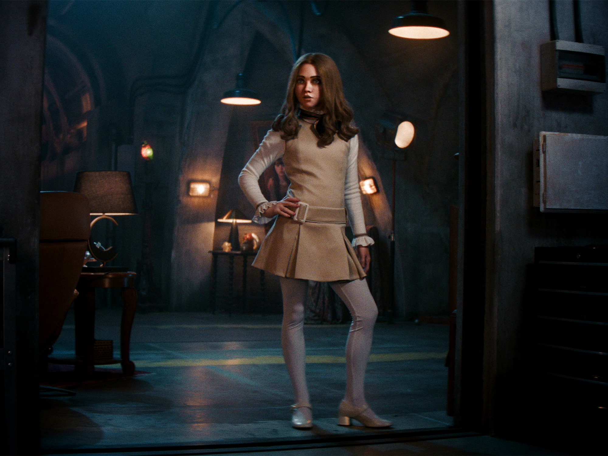 M3gan in a beige outfit standing in dimly lit room with lamps.