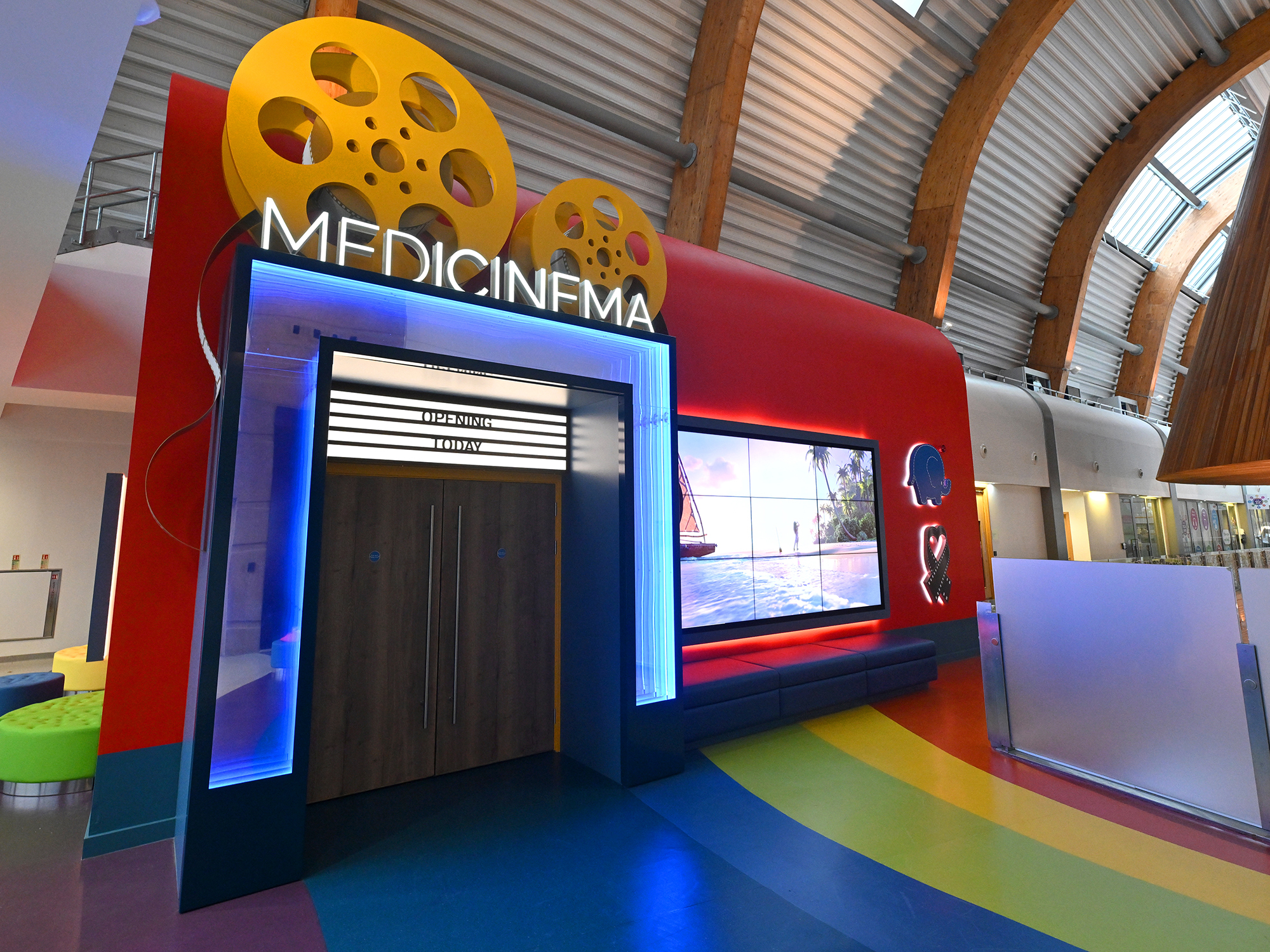 A large, brightly coloured structure with the text "MEDICINFMA" displayed prominently. The structure features a yellow film reel design on the top and a blue and red colour scheme. The floor in front of the structure is colourful and tiled.