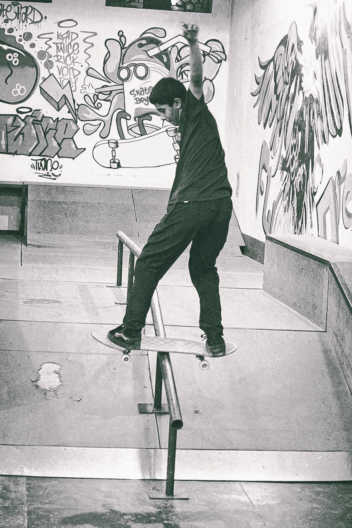 Person skateboarding on concrete ramp with graffiti-covered walls in background, black and white image with grainy texture.