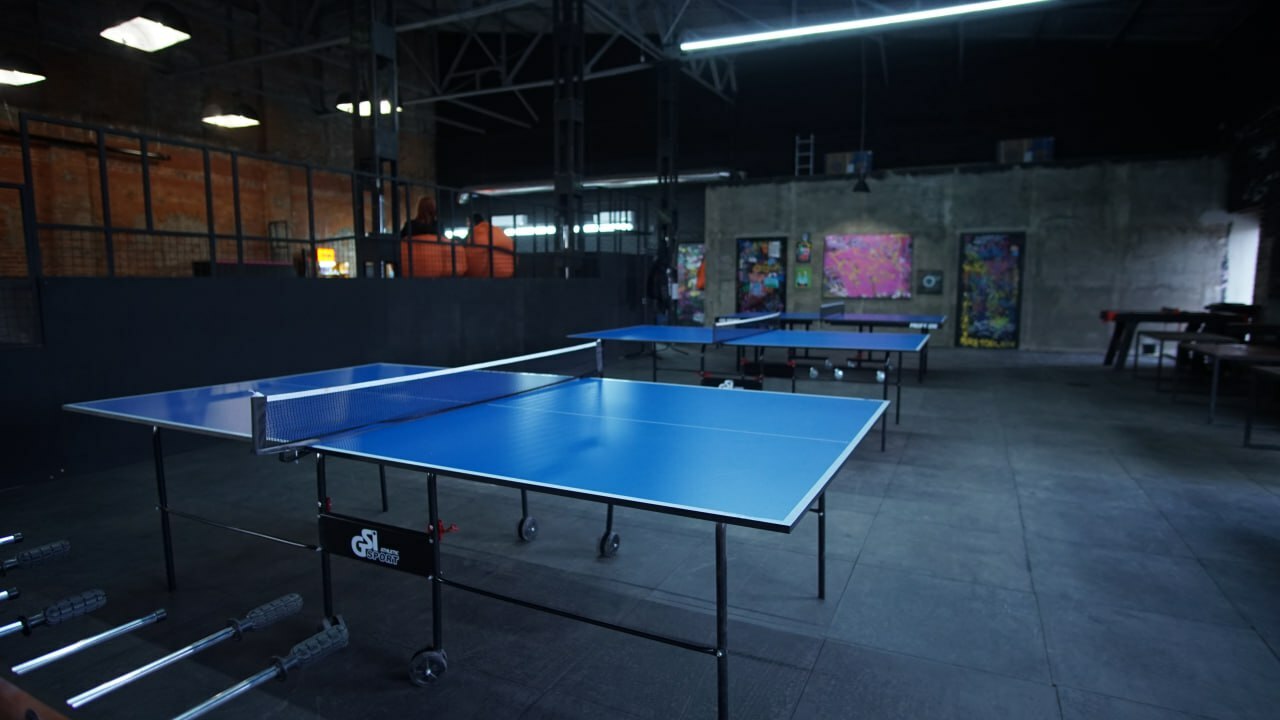Blue ping pong tables in a dimly lit indoor recreation area.