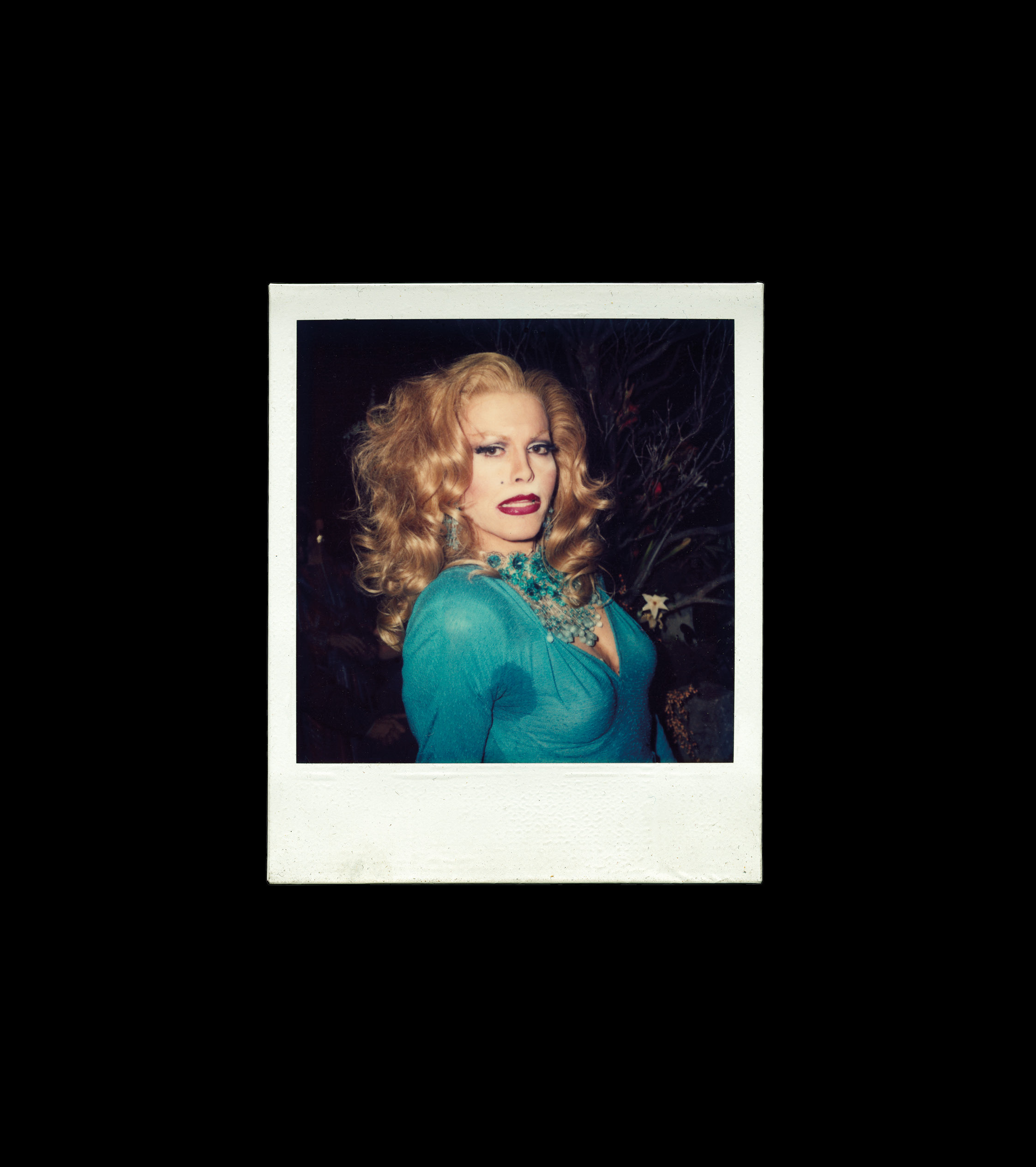 Curly-haired woman in teal blue dress against dark backdrop.