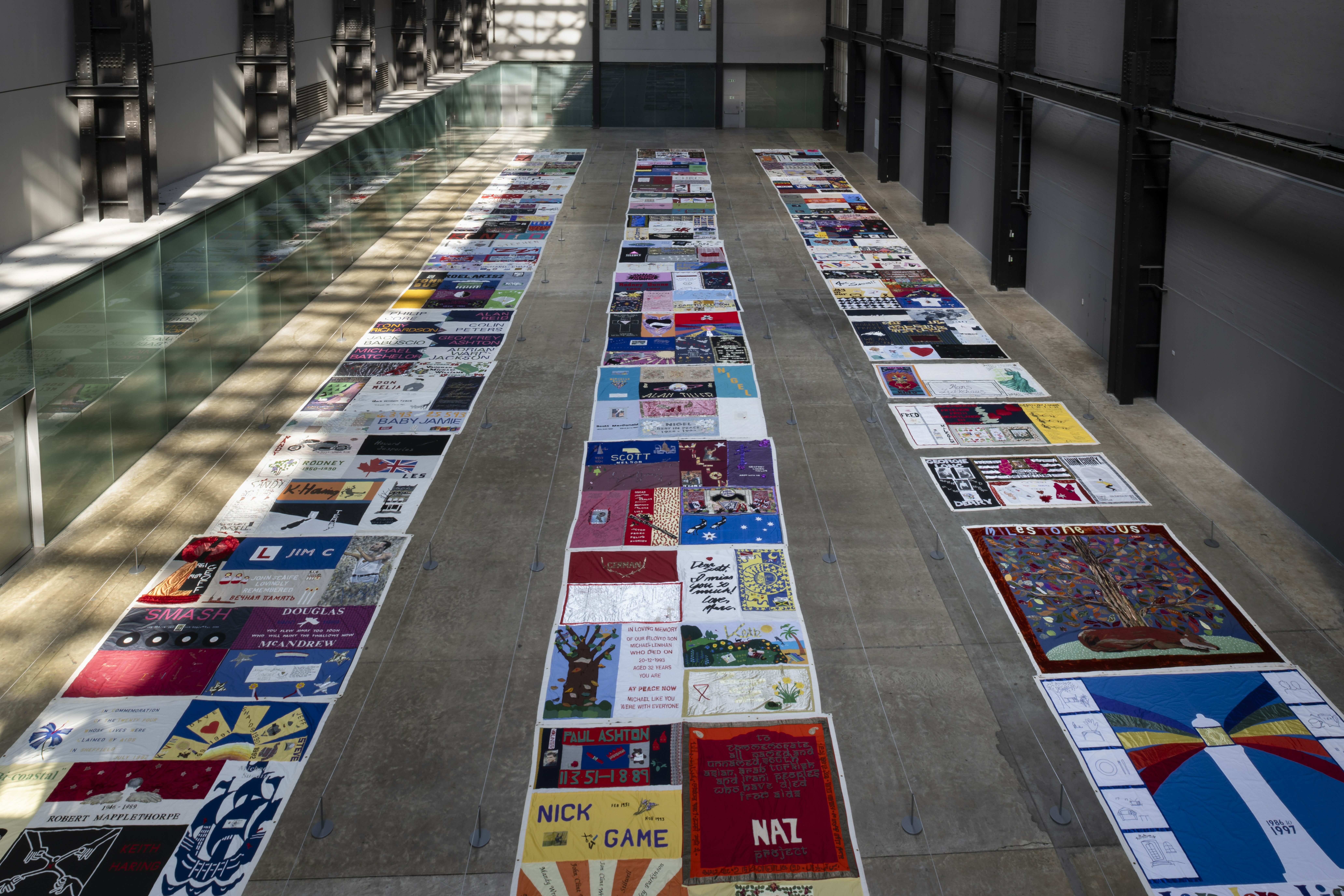 Colourful collage of album covers and record sleeves on display in a gallery or museum setting, with glass panels on either side reflecting the vibrant arrangement.
