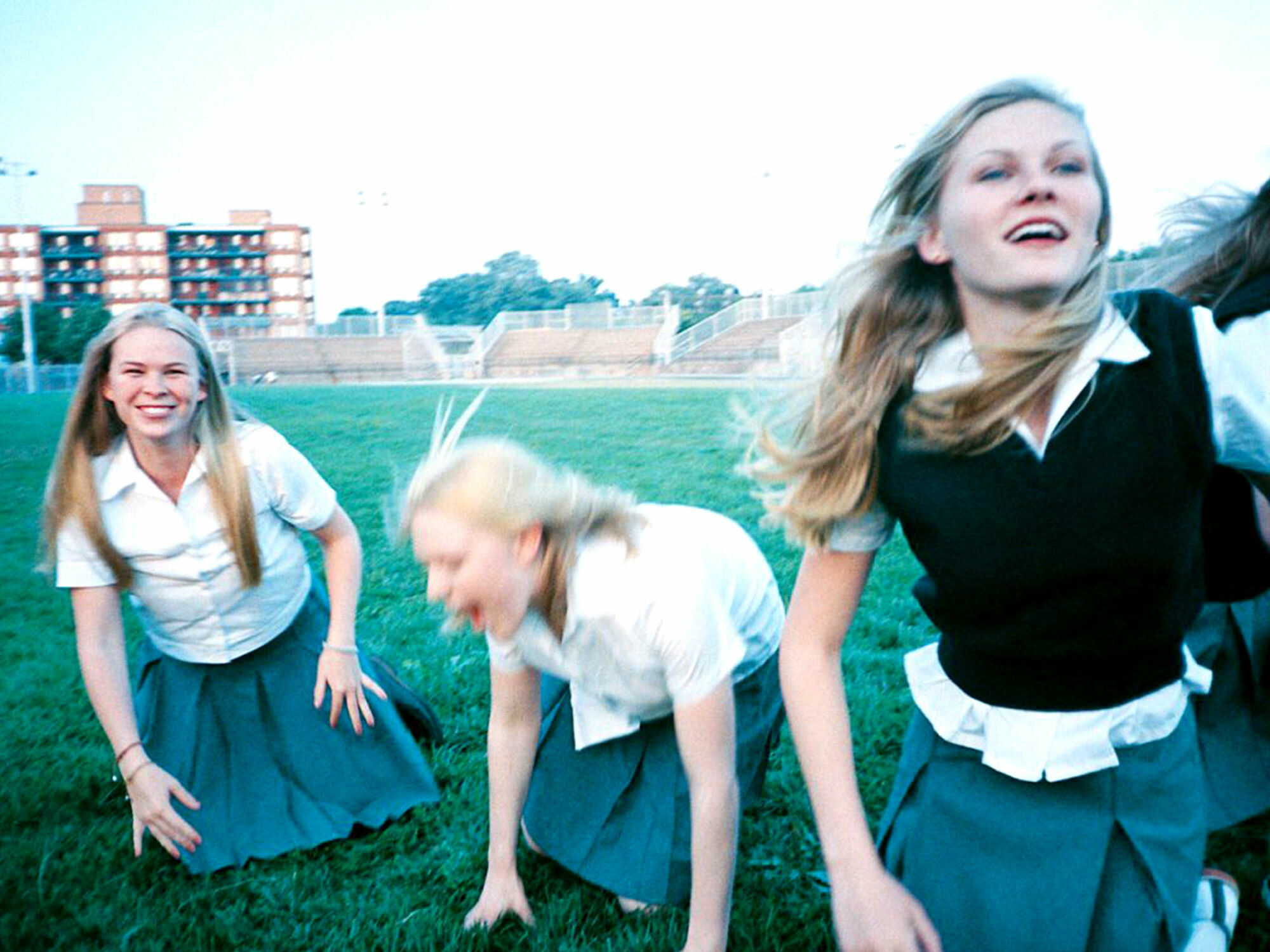 Three young women in school uniforms laughing and playing on a grassy field.