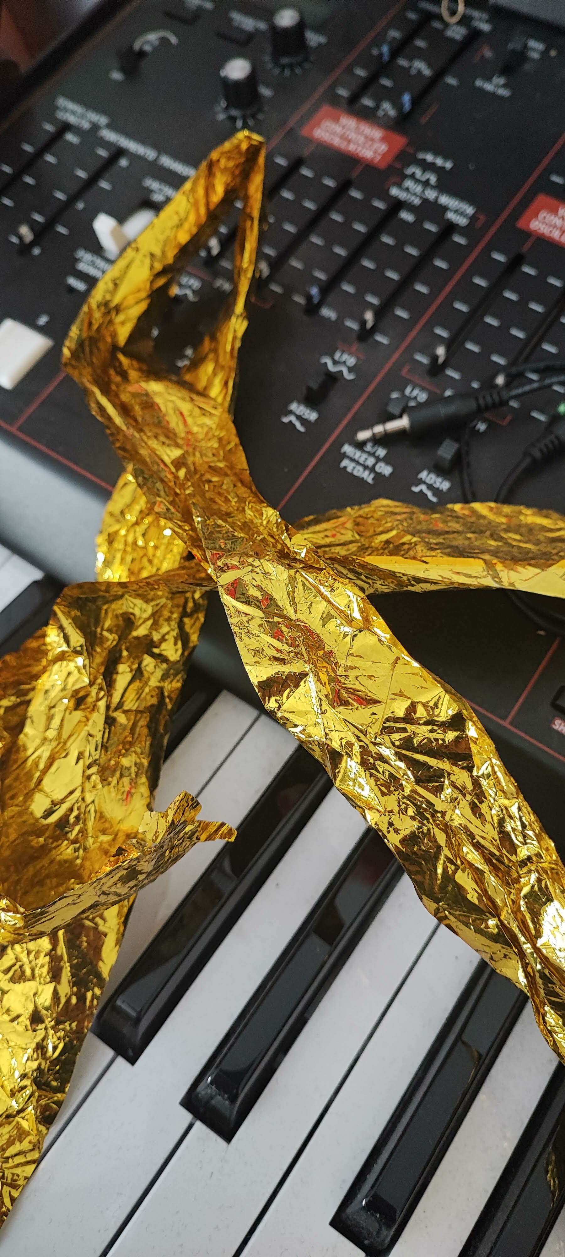 Crumpled golden foil ribbon draped across black and white piano keys with audio mixing console in background.