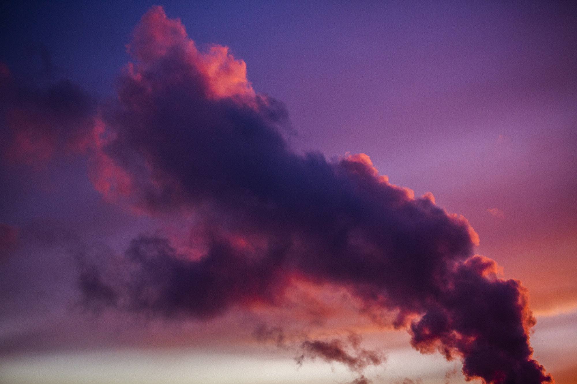 Dramatic dark clouds tinged with red and purple against a deep blue sky at sunset.