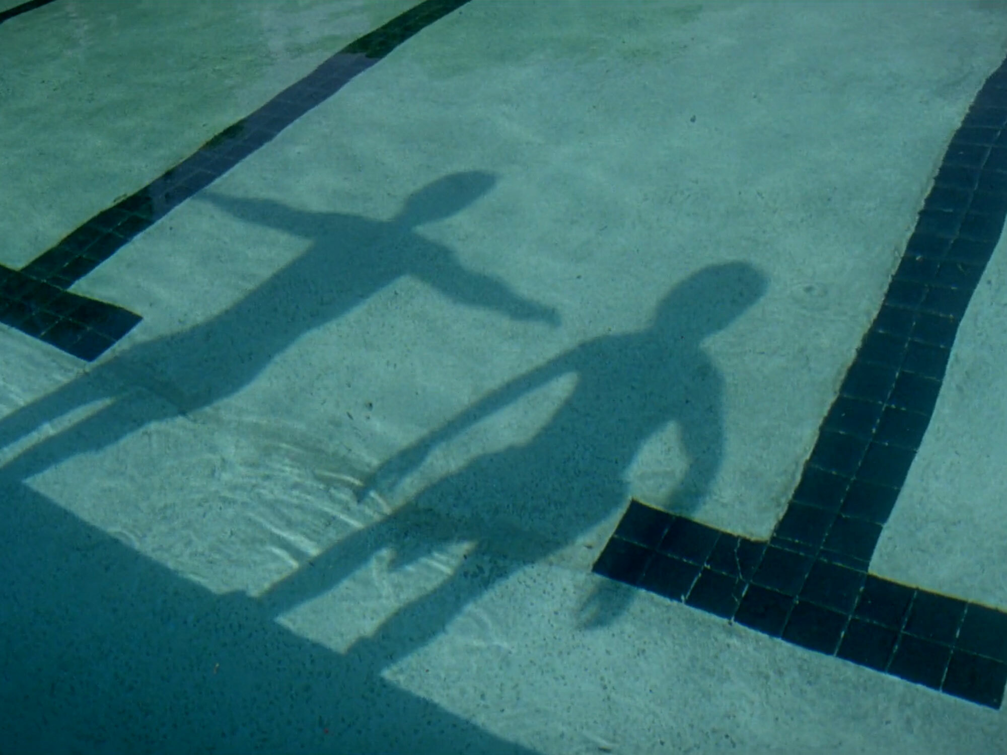Shadow silhouettes of two people reflected on the water of a swimming pool