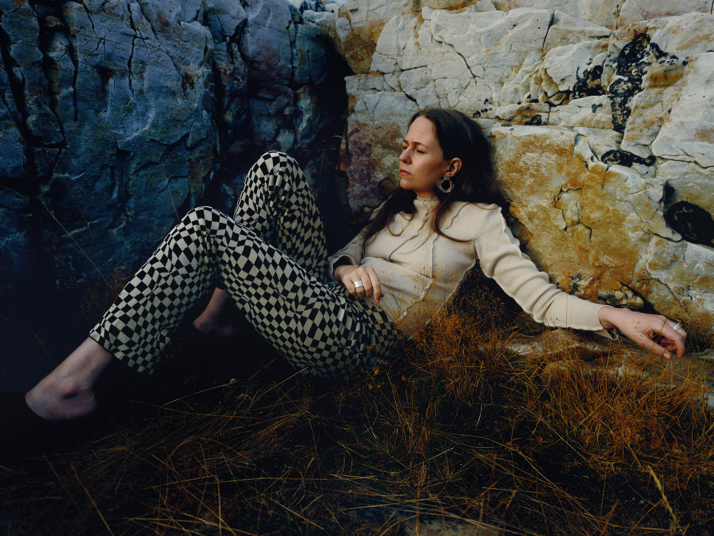 Alice Boman leaning against some rocks, lying on the floor wearing a grey top and black and white checked trousers